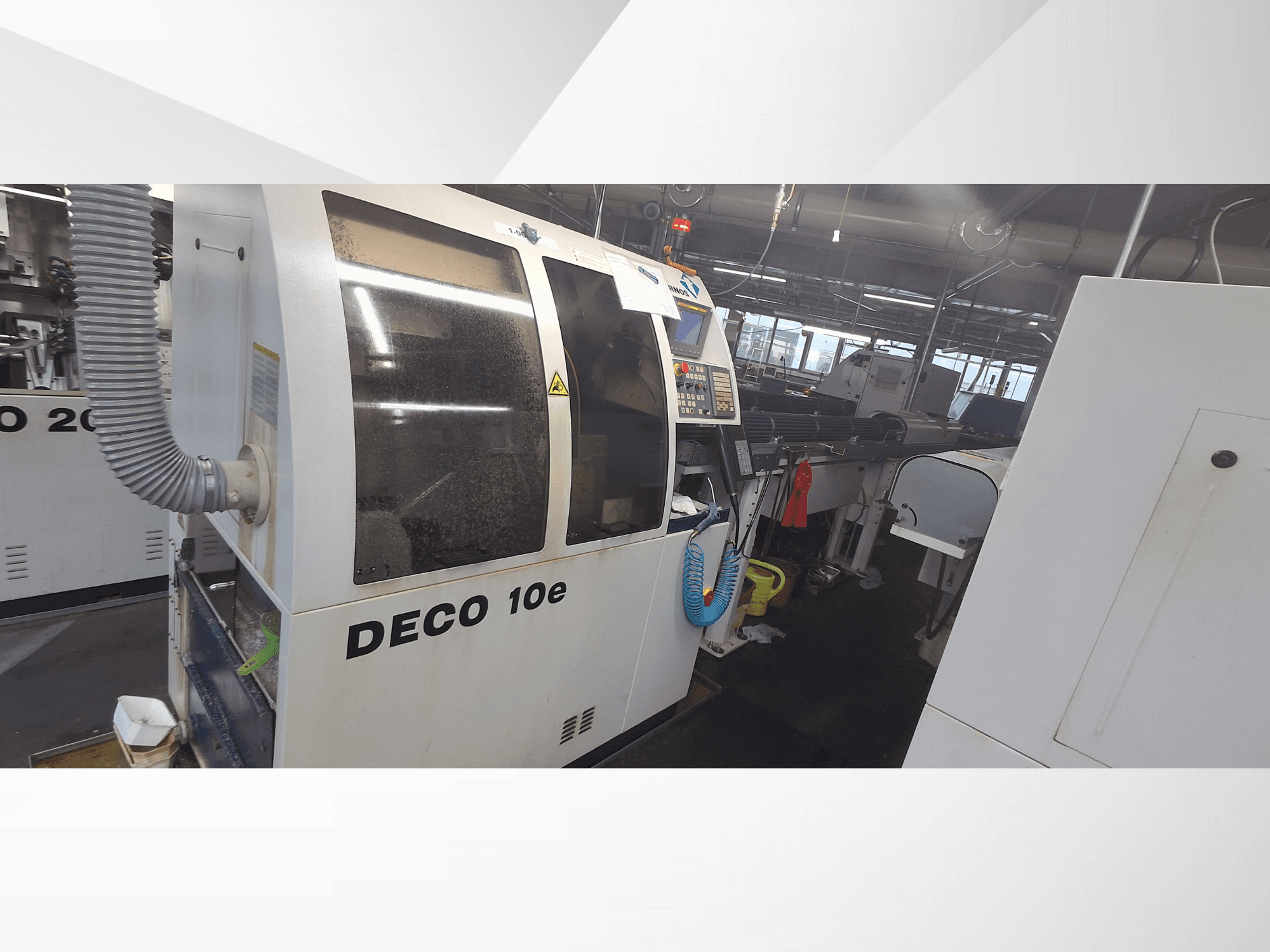DECO 10e machine in een werkplaats; zijaanzicht met bedieningspaneel en ventilatieslang, met vage machines op de achtergrond.