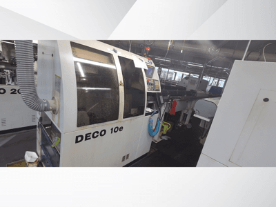 DECO 10e machine in een werkplaats; zijaanzicht met bedieningspaneel en ventilatieslang, met vage machines op de achtergrond.
