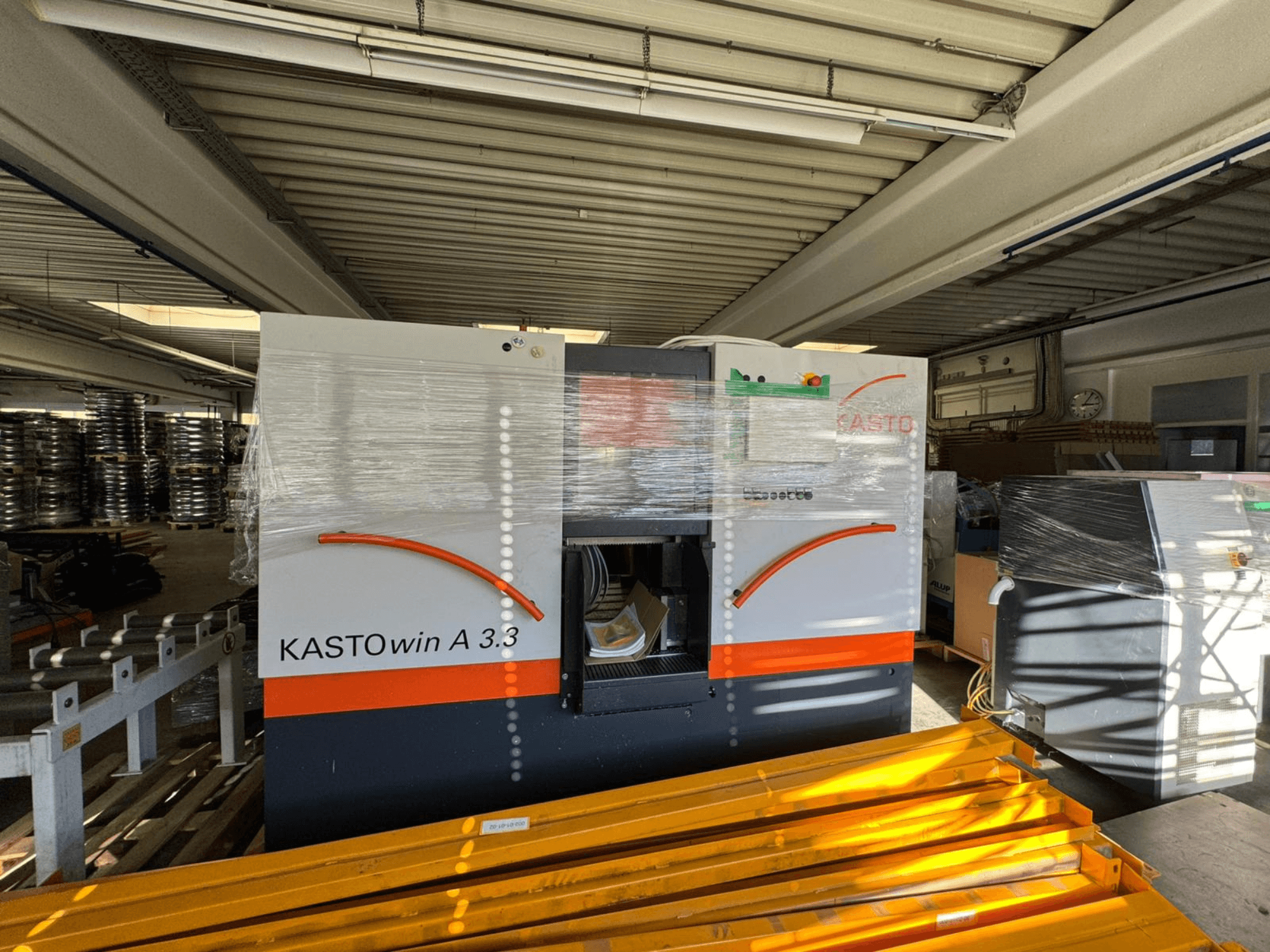 KASTO win A 3.3 metaalbandzaag in vooraanzicht, ter bescherming ingepakt, waarbij de bedieningselementen en de omliggende apparatuur zichtbaar zijn.