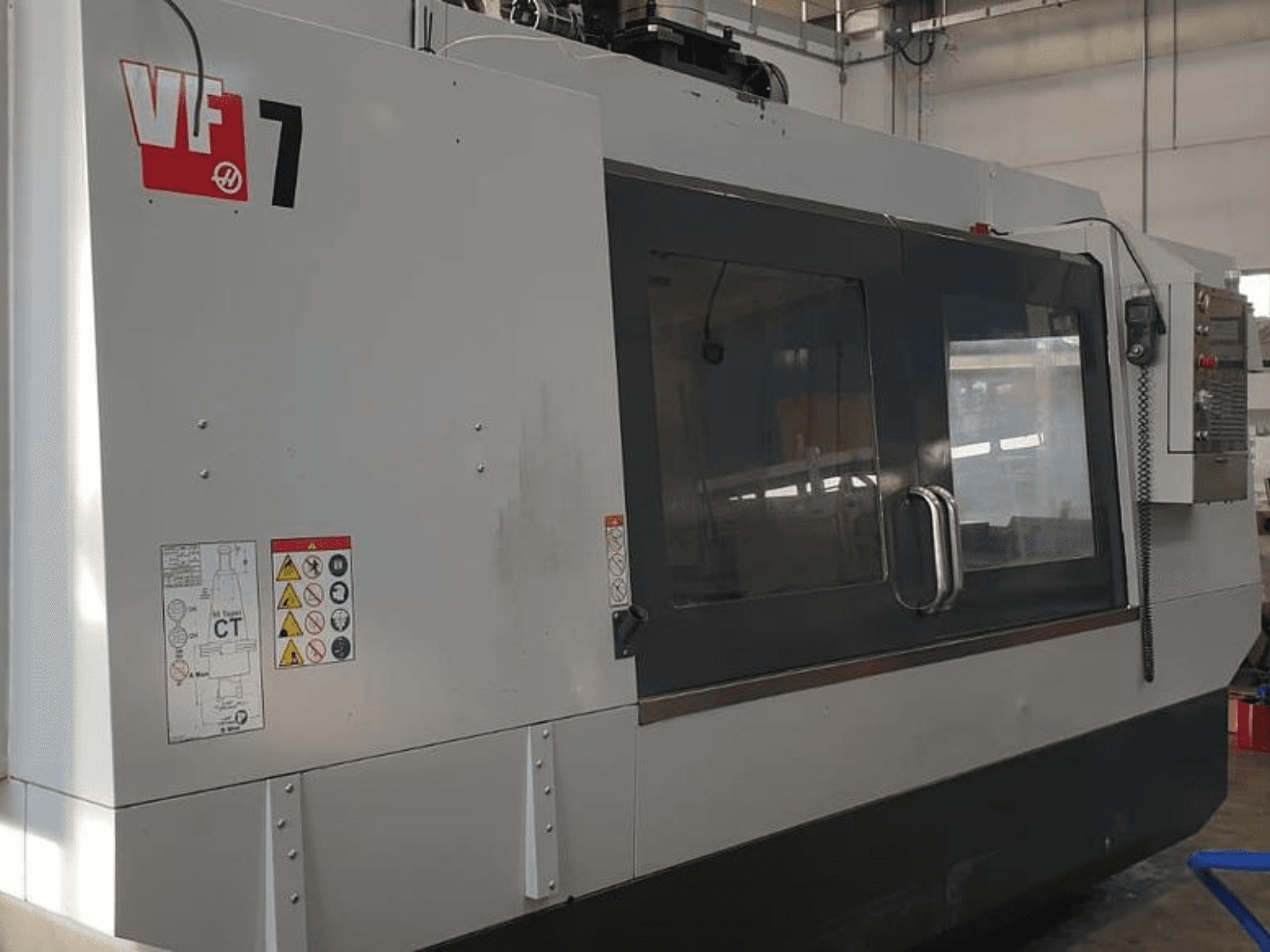 Haas VF-7 CNC machine in zijaanzicht, met een metaalgrijze afwerking, bedieningspaneel en veiligheidslabels.