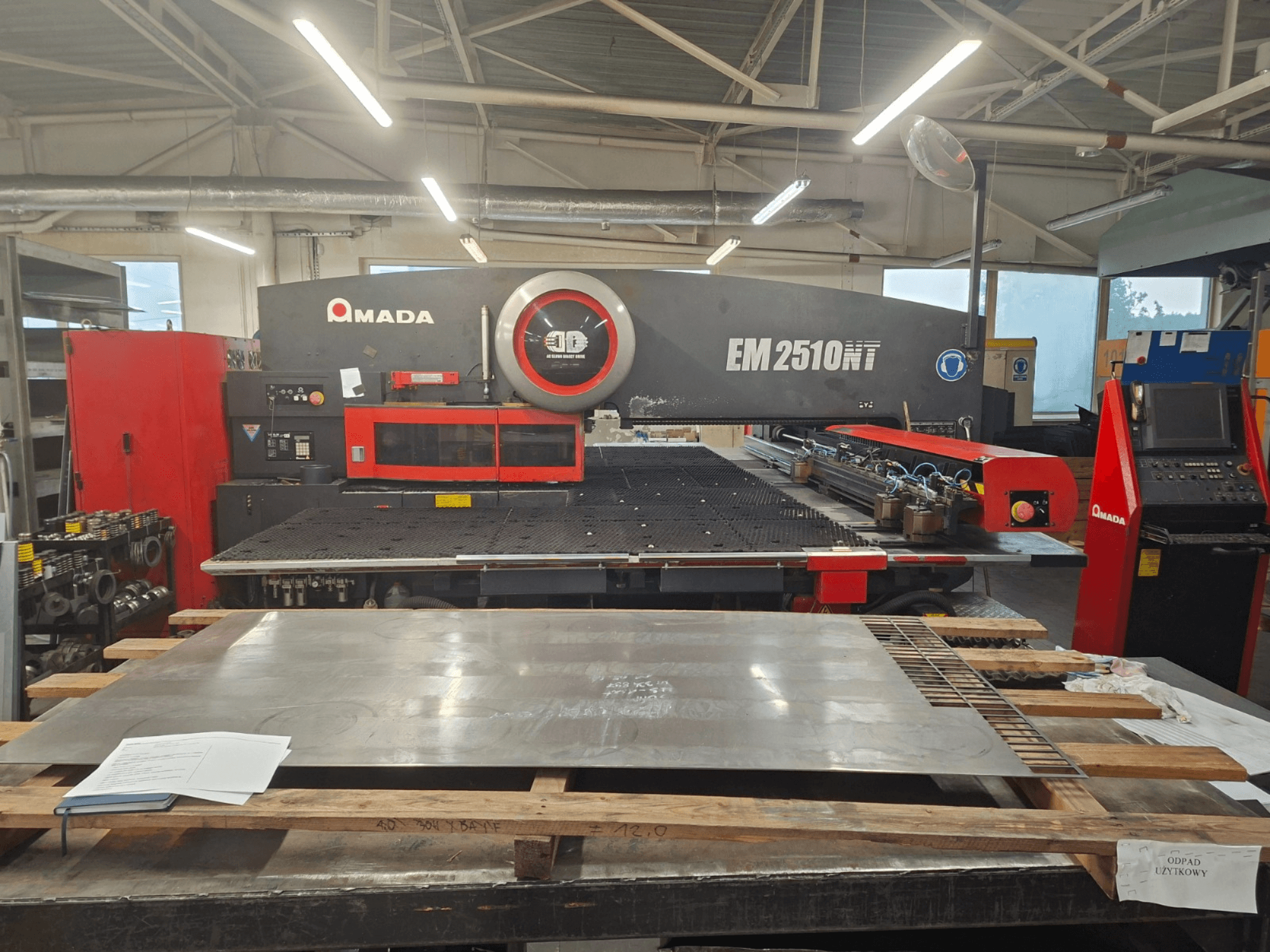 Vooraanzicht van de AMADA EM 2510NT revolverstansmachine, met metalen plaat en bedieningspaneel zichtbaar in een werkplaats.