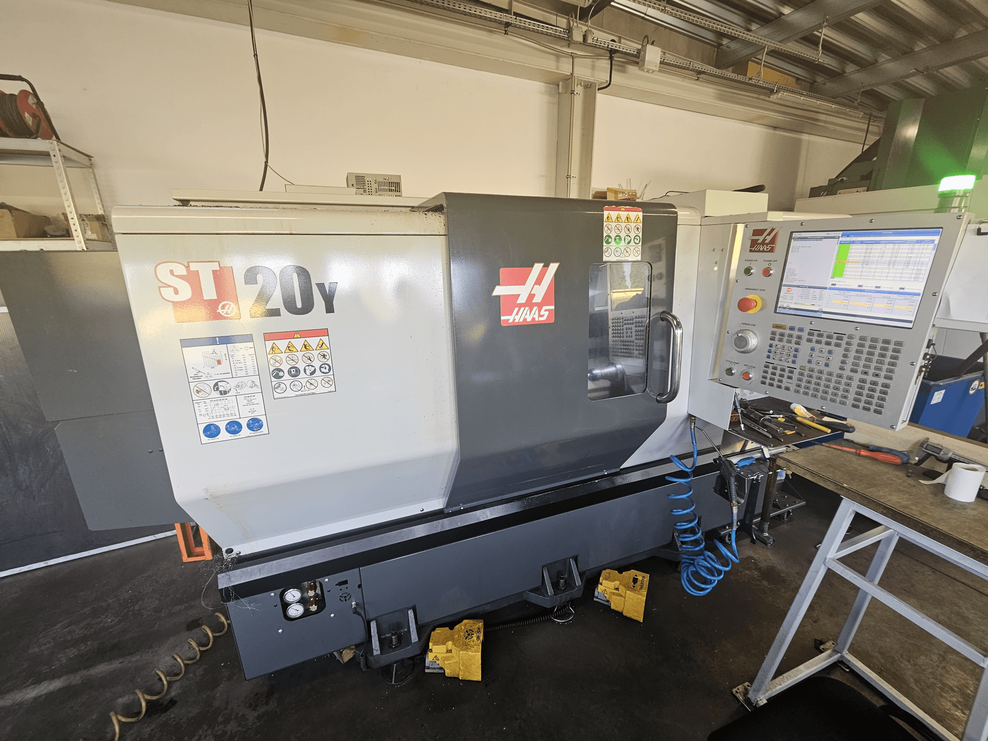Haas ST-20Y CNC draaibank in vooraanzicht met bedieningspaneel; inclusief veiligheidslabels en details van de luchtslang aan de zijkant.