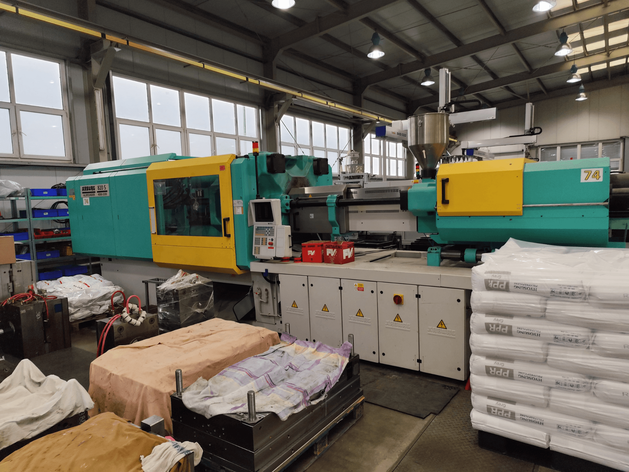 Spuitgietmachine van Arburg, vooraanzicht, groenblauwe en gele buitenkant, met gereedschap en materialen in de buurt.