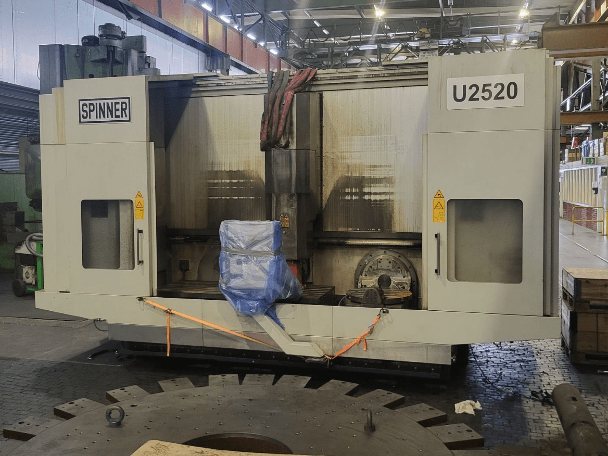 Verticaal bewerkingscentrum SPINNER U5-2520, gezien vanaf de voorkant, met een afgedekte werktafel en veiligheidsstickers.