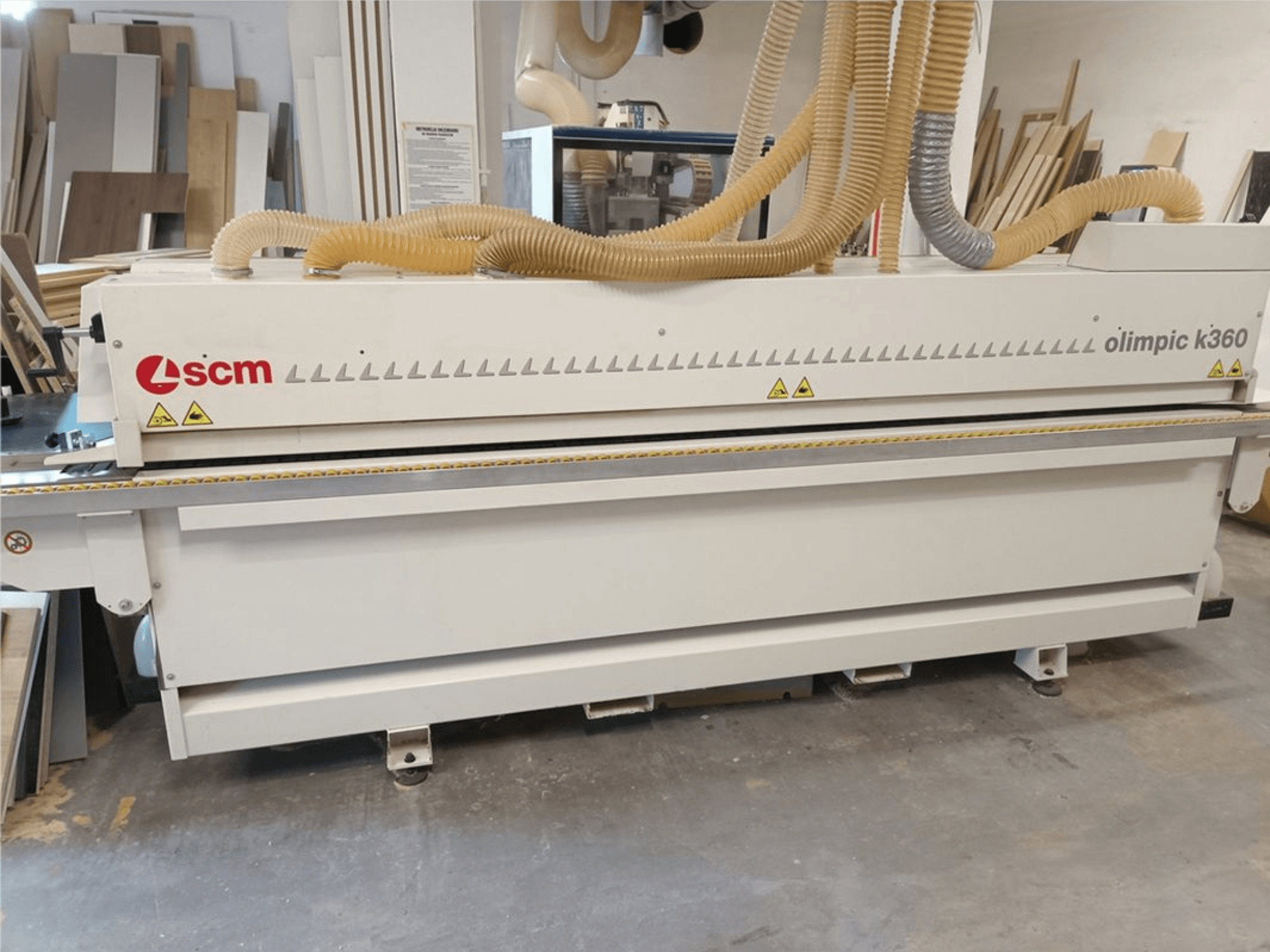 SCM Olimpic K360 T-ER1 kantenlijmmachine in een werkplaats, vooraanzicht met stofafzuigslangen en waarschuwingslabels.
