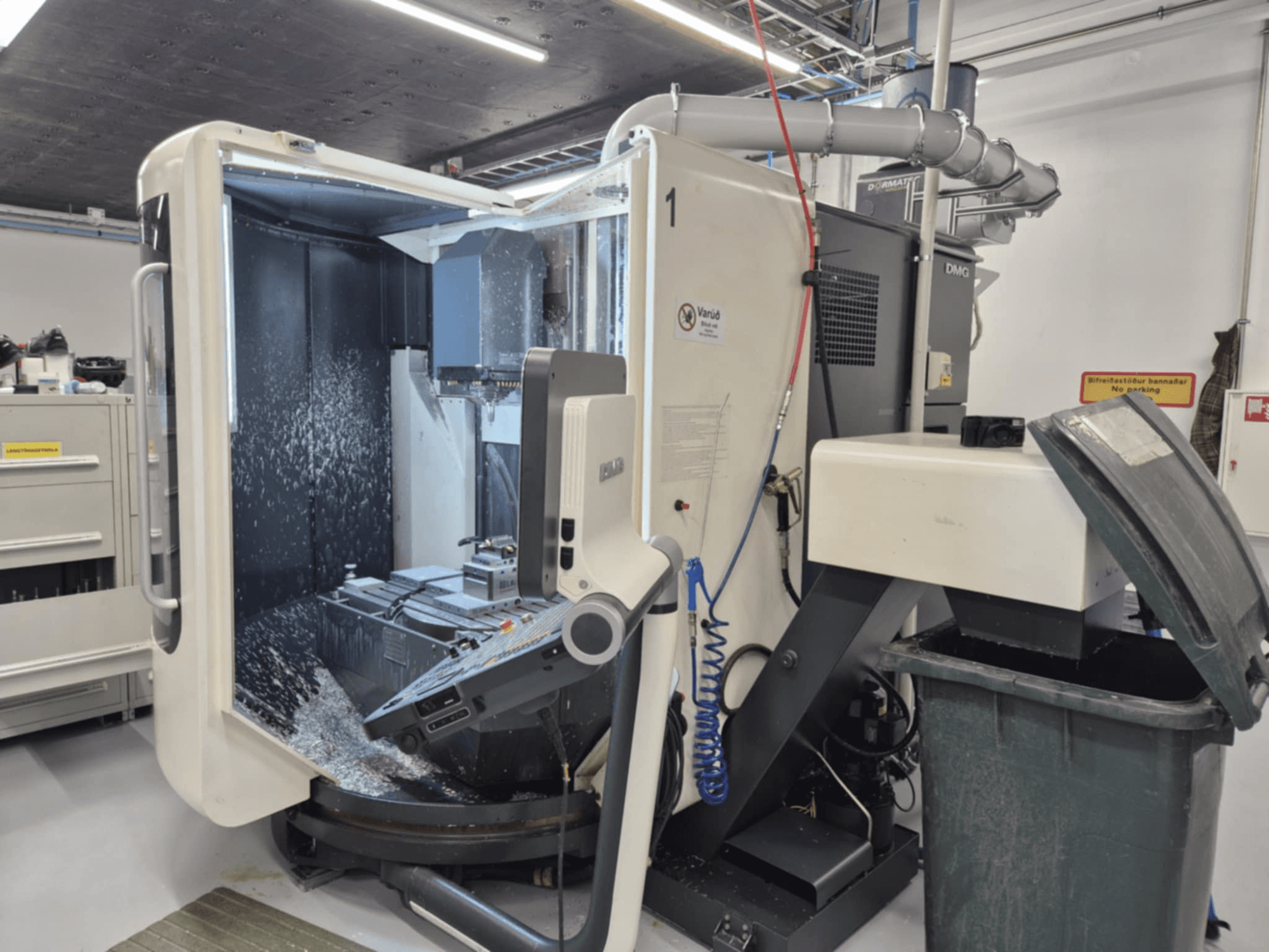 Open DMG freesmachine met koelvloeistofnevel, met metaalschilfers en gereedschapsbediening, gezien vanaf de voorkant.