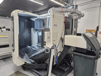 Open DMG freesmachine met koelvloeistofnevel, met metaalschilfers en gereedschapsbediening, gezien vanaf de voorkant.