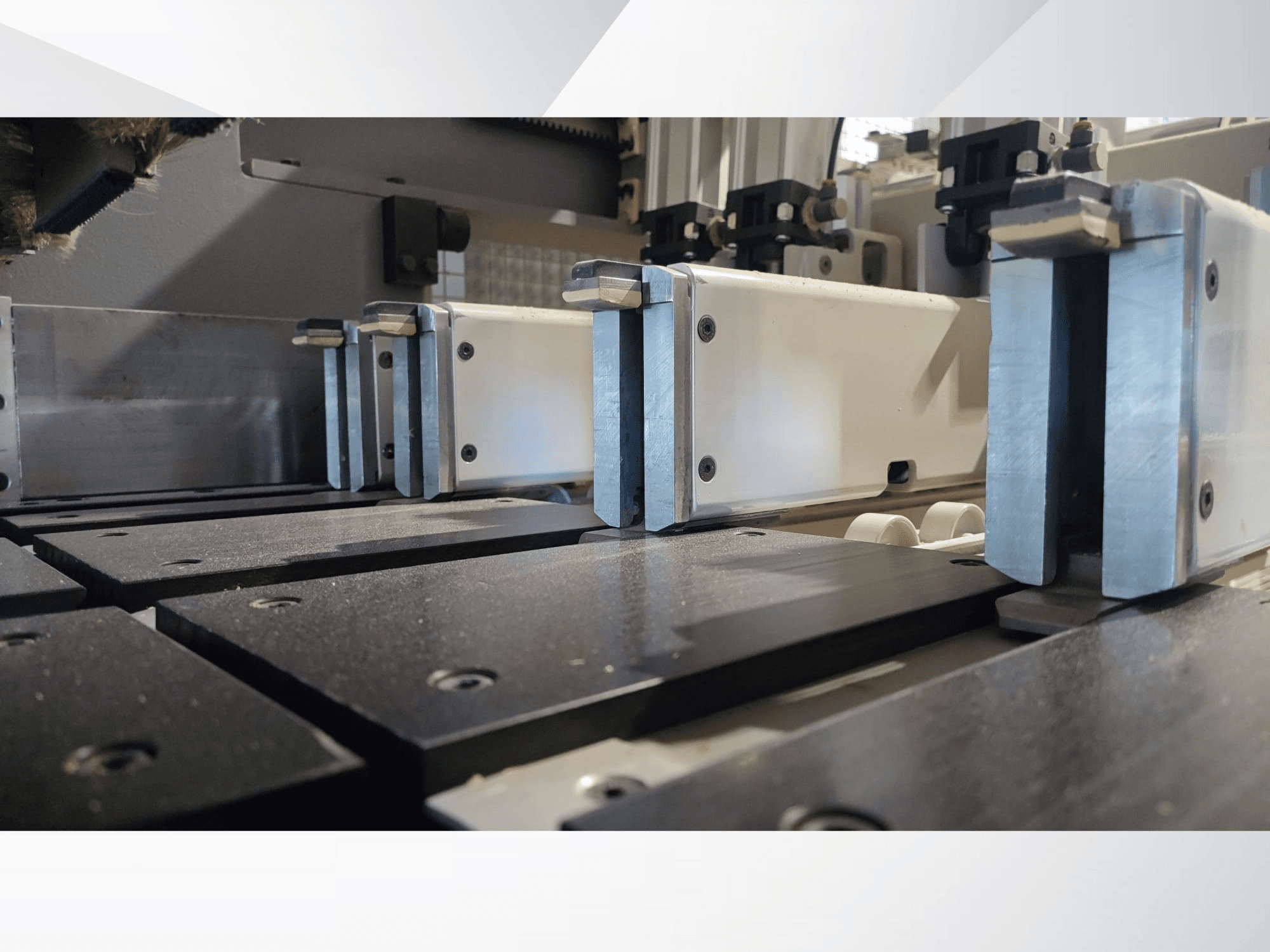 Close-up van het klemmechanisme van een precisiemachine met metalen bekken, met zwarte werkoppervlakken en zichtbare geleiderails.