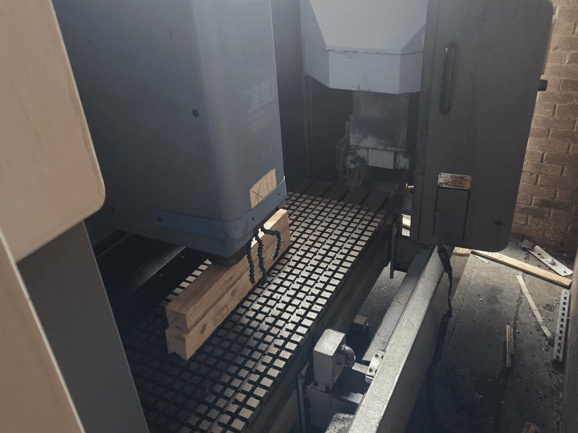 Vooraanzicht CNC machine met houten planken op een roostertafel, met aan de zijkant gereedschap en bedieningselementen.