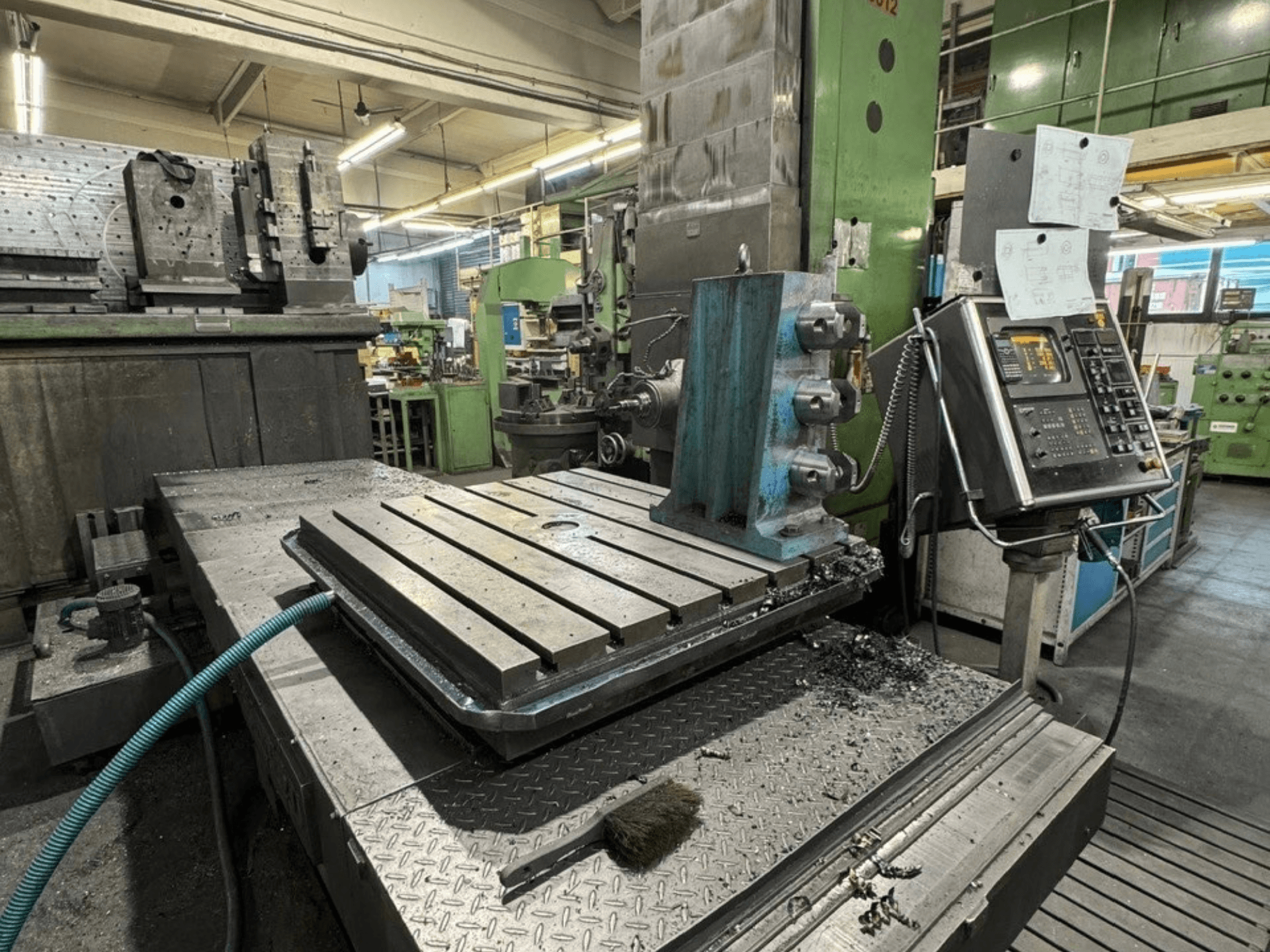 JUARISTI 12/TS1.7-boormachine in een werkplaats, zijaanzicht met metalen tafel met groeven en bedieningspaneel ernaast.