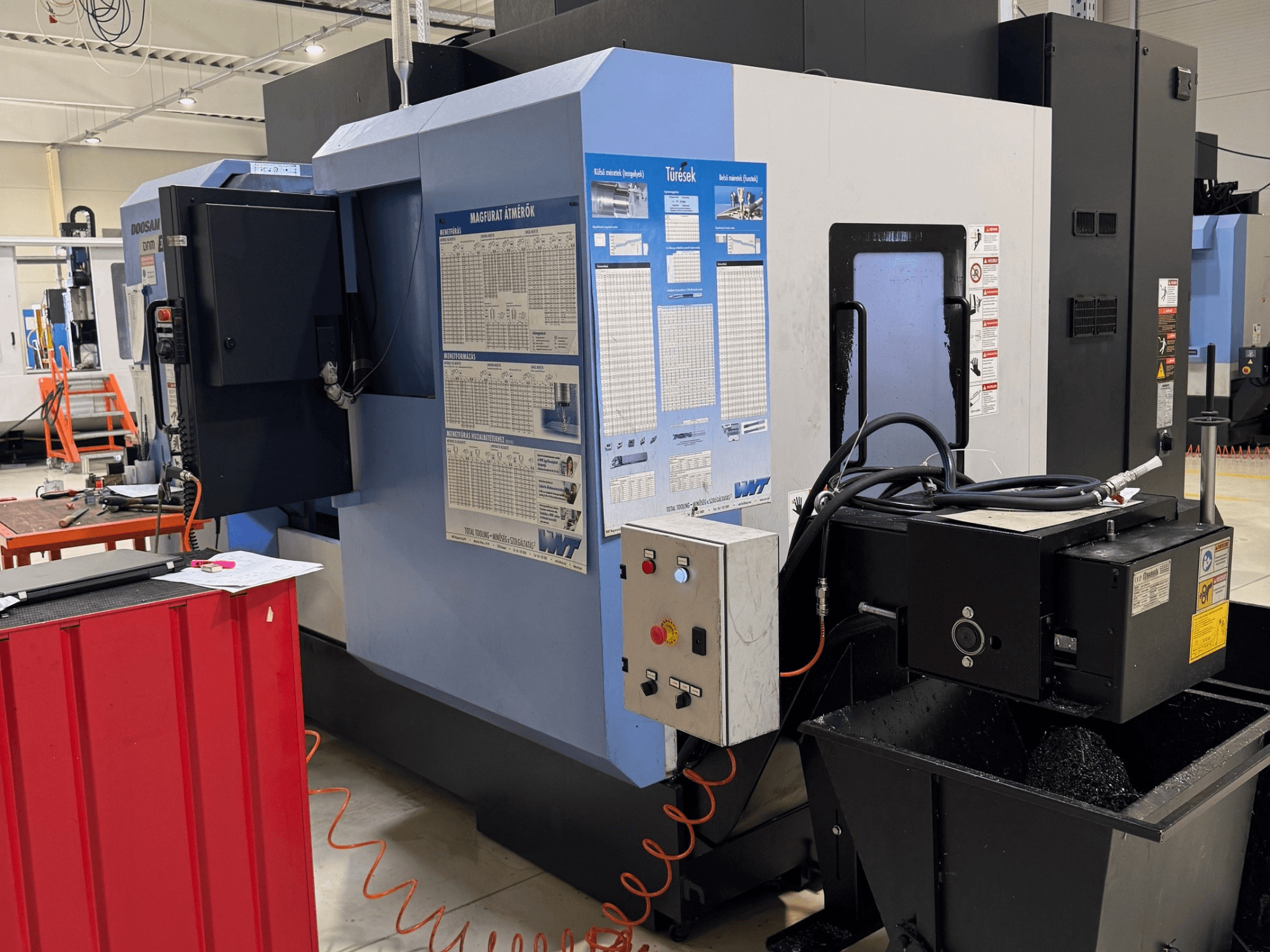 DOOSAN DNM350/5AX frees- en draaicentrum, zijaanzicht met het bedieningspaneel en de koelvloeistoftank, waarbij de functionele details zichtbaar zijn.
