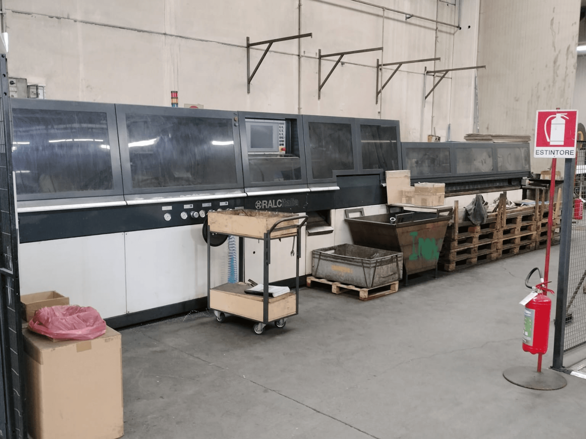 RALC industriële machine in een fabrieksomgeving, vooraanzicht, met bedieningspaneel zichtbaar; houten pallets en brandblusser dichtbij.