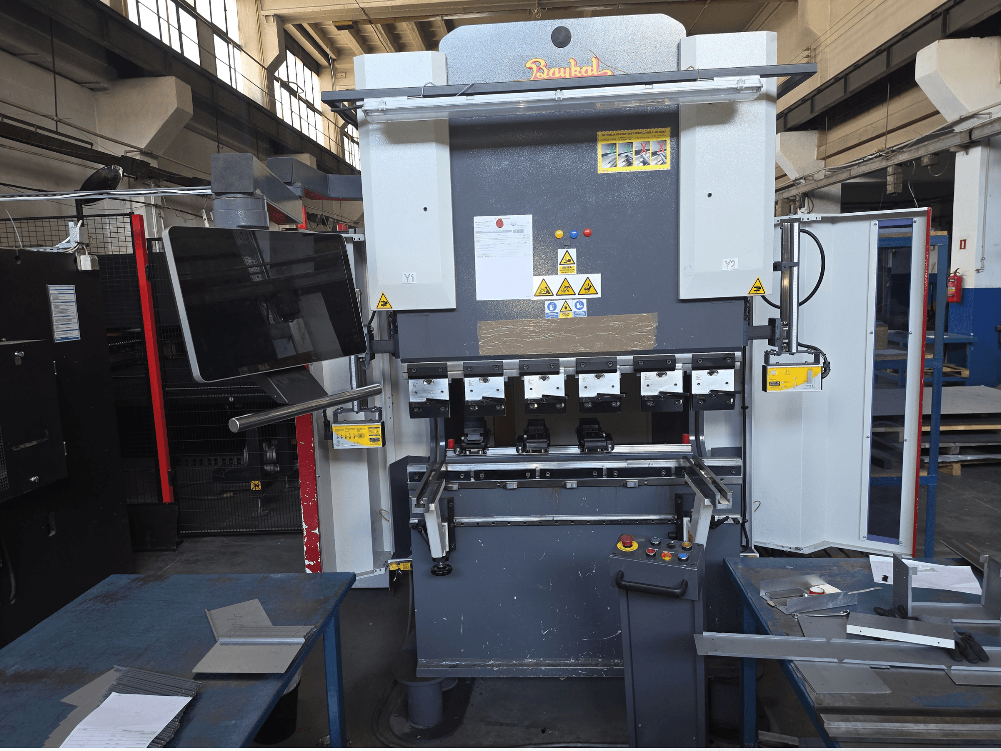 Baykal APHS 125040 kantpers, vooraanzicht, met het bedieningspaneel en de veiligheidsvoorzieningen in beeld, met materialen op een blauwe werktafel.