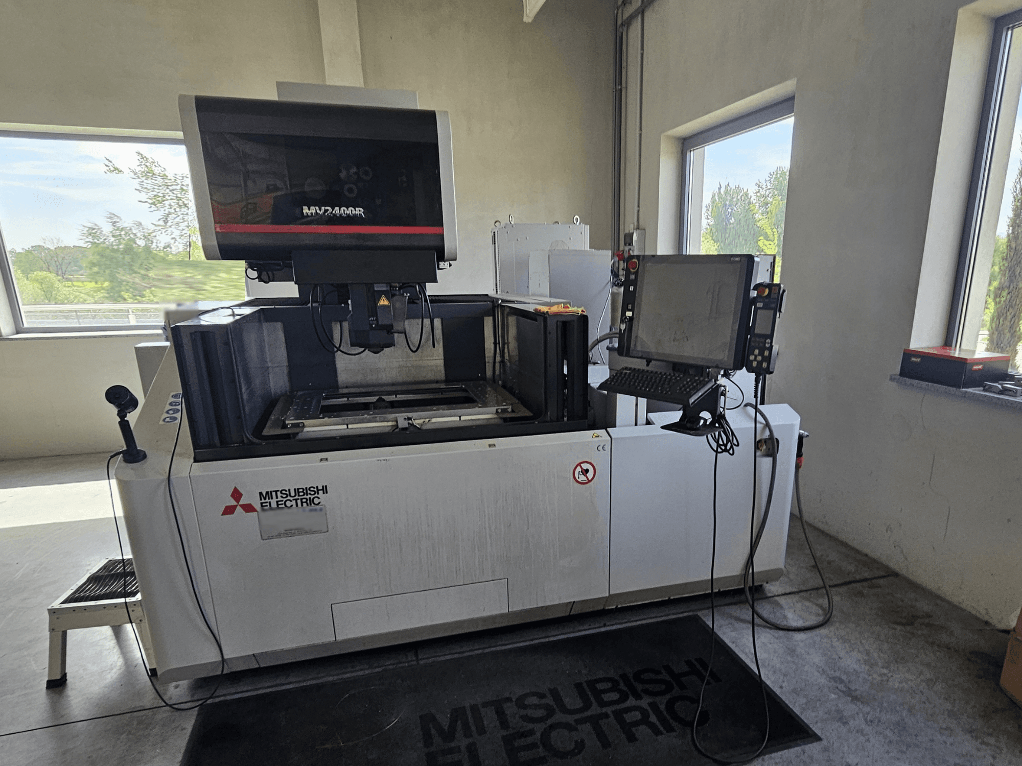 Mitsubishi MV2400R draadvonkmachine in een werkplaats, met een touchscreen bedieningspaneel en werkruimte.
