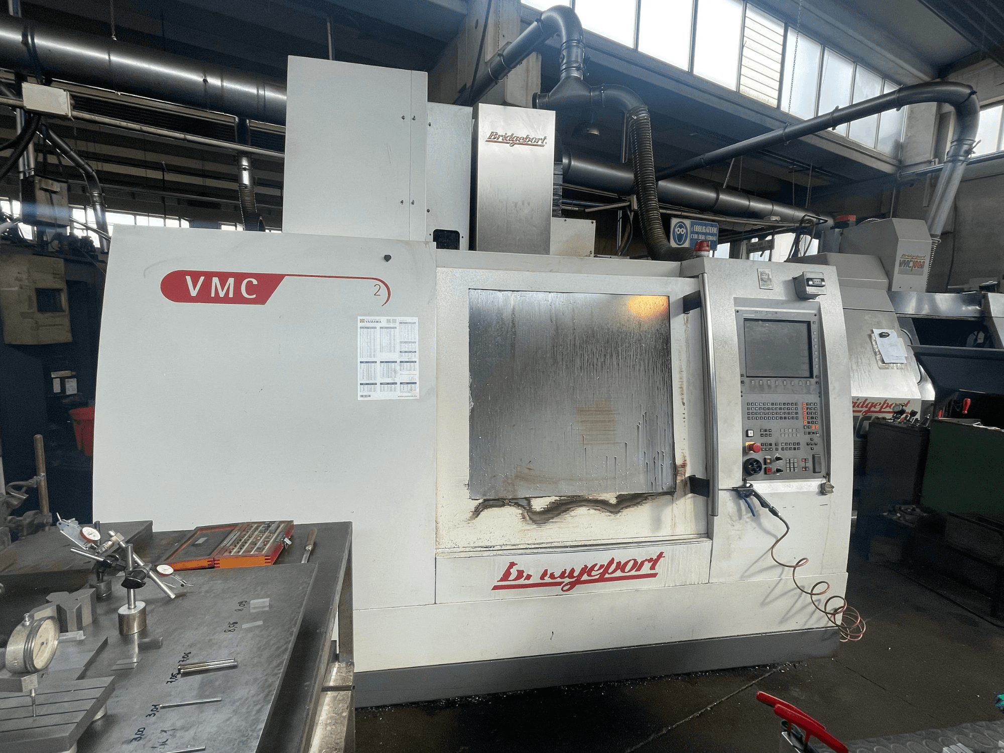 Verticaal bewerkingscentrum Bridgeport VCM 800-30 in een werkplaats, met bedieningspaneel en gereedschapstafel. Vooraanzicht met zichtbare details.