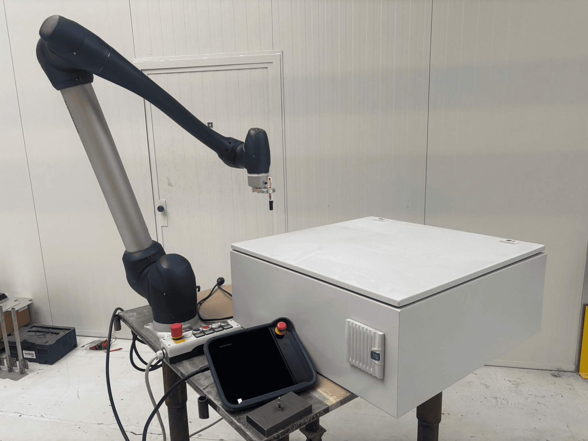 DOOSAN M0617 collaboratieve robot in zijaanzicht, met robotarm uitgestrekt boven een besturingsinterface en een witte doos op een tafel.