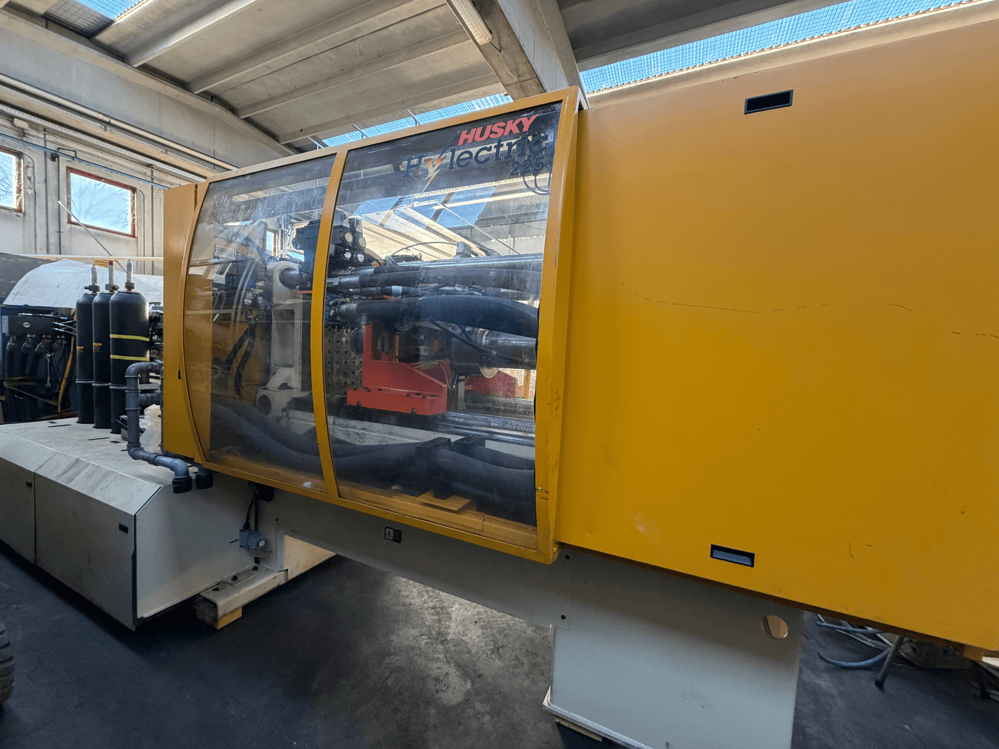 Husky HL225 RS65 elektrische spuitgietmachine, vooraanzicht met gele behuizing, zichtbaar bedieningspaneel en hydraulische componenten.