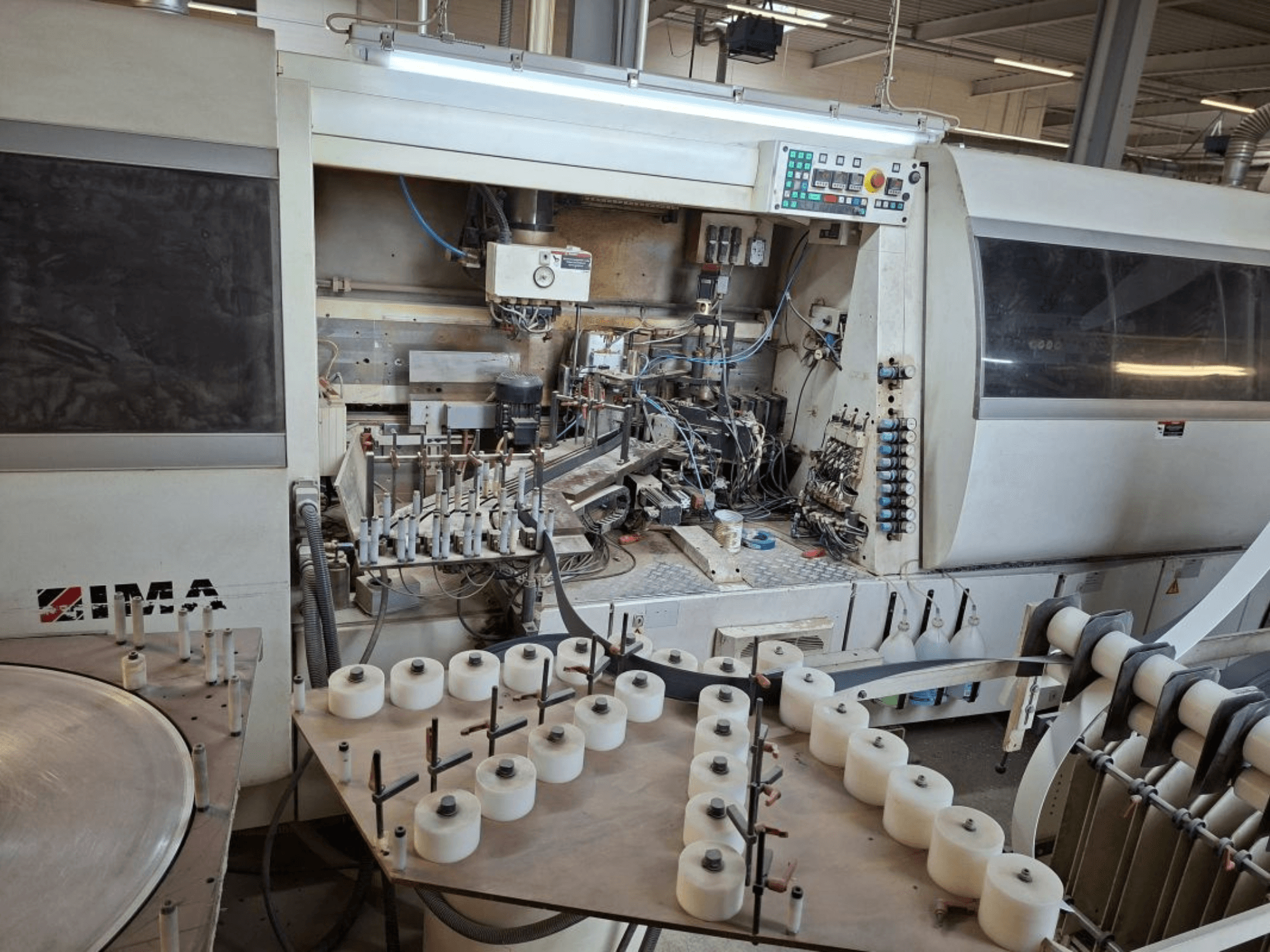 IMA machines gezien vanaf de zijkant, met complexe mechanische onderdelen en een ronde tafel met witte spoelen.