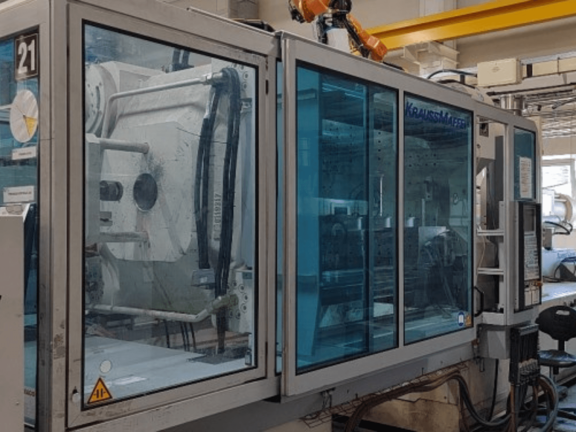 Krauss Maffei KM 575-2700 C2 hydraulische spuitgietmachine, zijaanzicht, met doorzichtige veiligheidspanelen en bedieningspaneel.