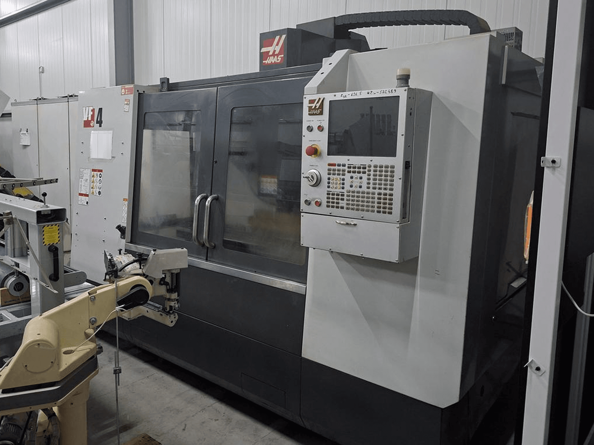 Haas VF-4 CNC freesmachine in vooraanzicht, met een numeriek besturingspaneel en robotarm voor automatisering.