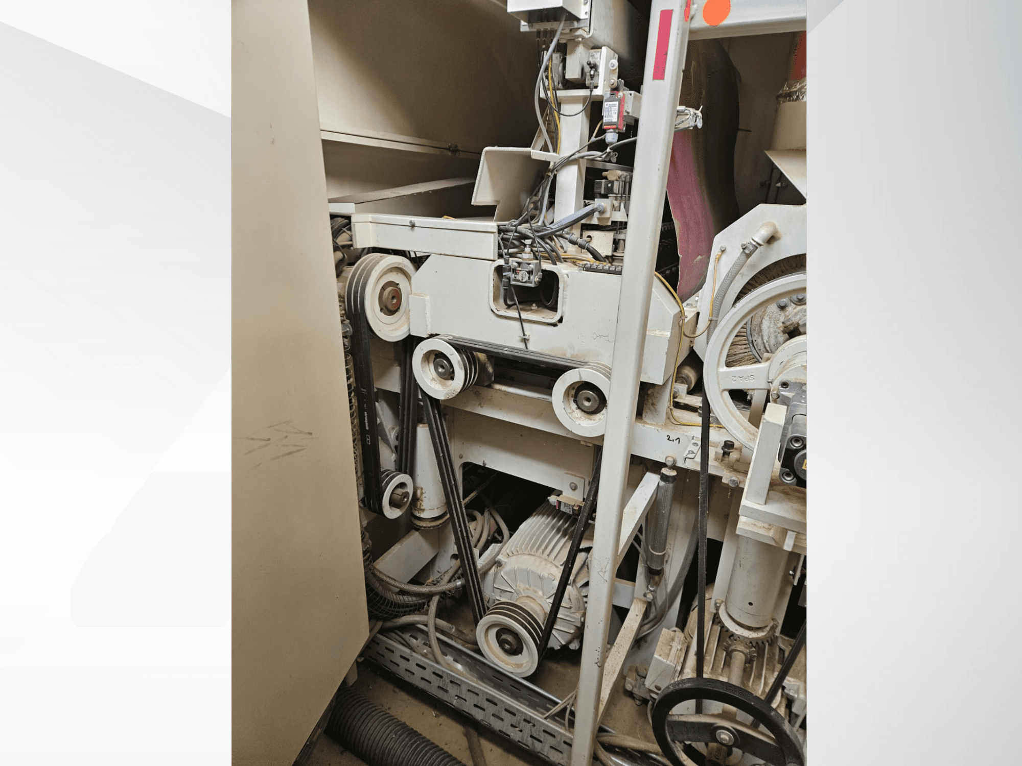 Industrieel machine-interieur met riemen en katrollen, met een motor en bedrading, gezien vanaf de zijkant.