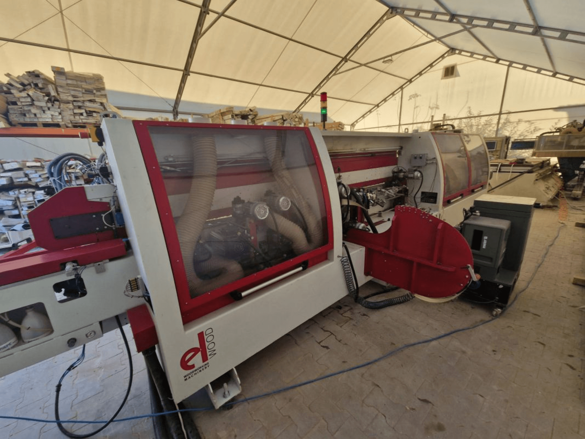 ELWOOD EDL SOFT kantenlijmmachine, zijaanzicht met stofafzuiging en bedieningselementen in een werkplaats met stapels hout.
