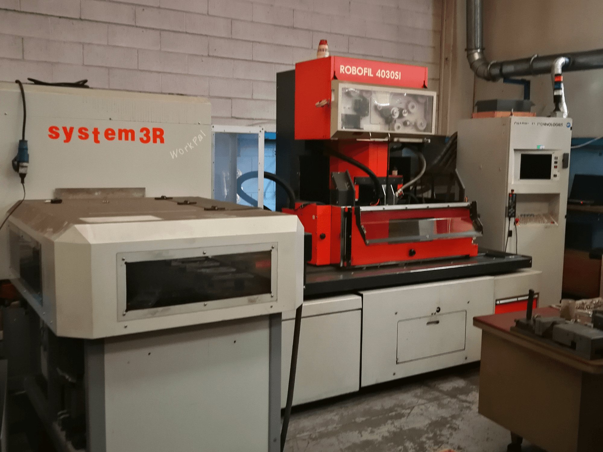 Vooraanzicht van CHARMILLES ROBOFIL 4030 Si draadvonkmachine, met een rood en grijs uiterlijk en aangrenzend system3R werkstation.