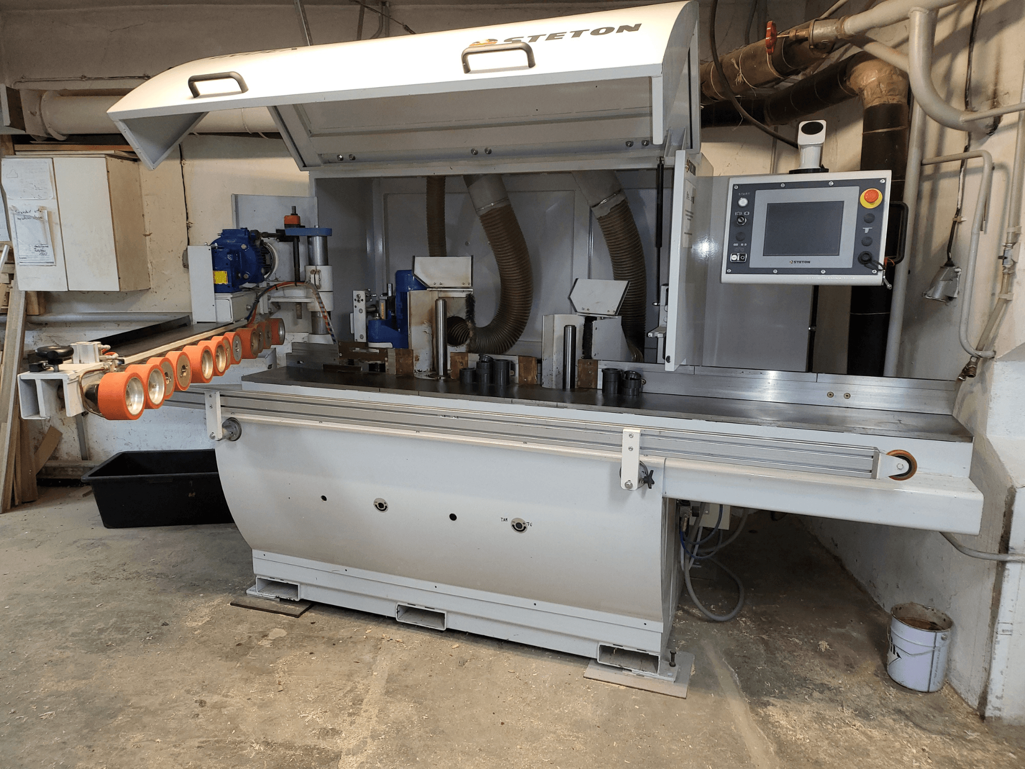 Een vooraanzicht van een Stetton houtbewerkingsmachine met een bedieningspaneel, aanvoerbuizen en verschillende stukken hout op de tafel.