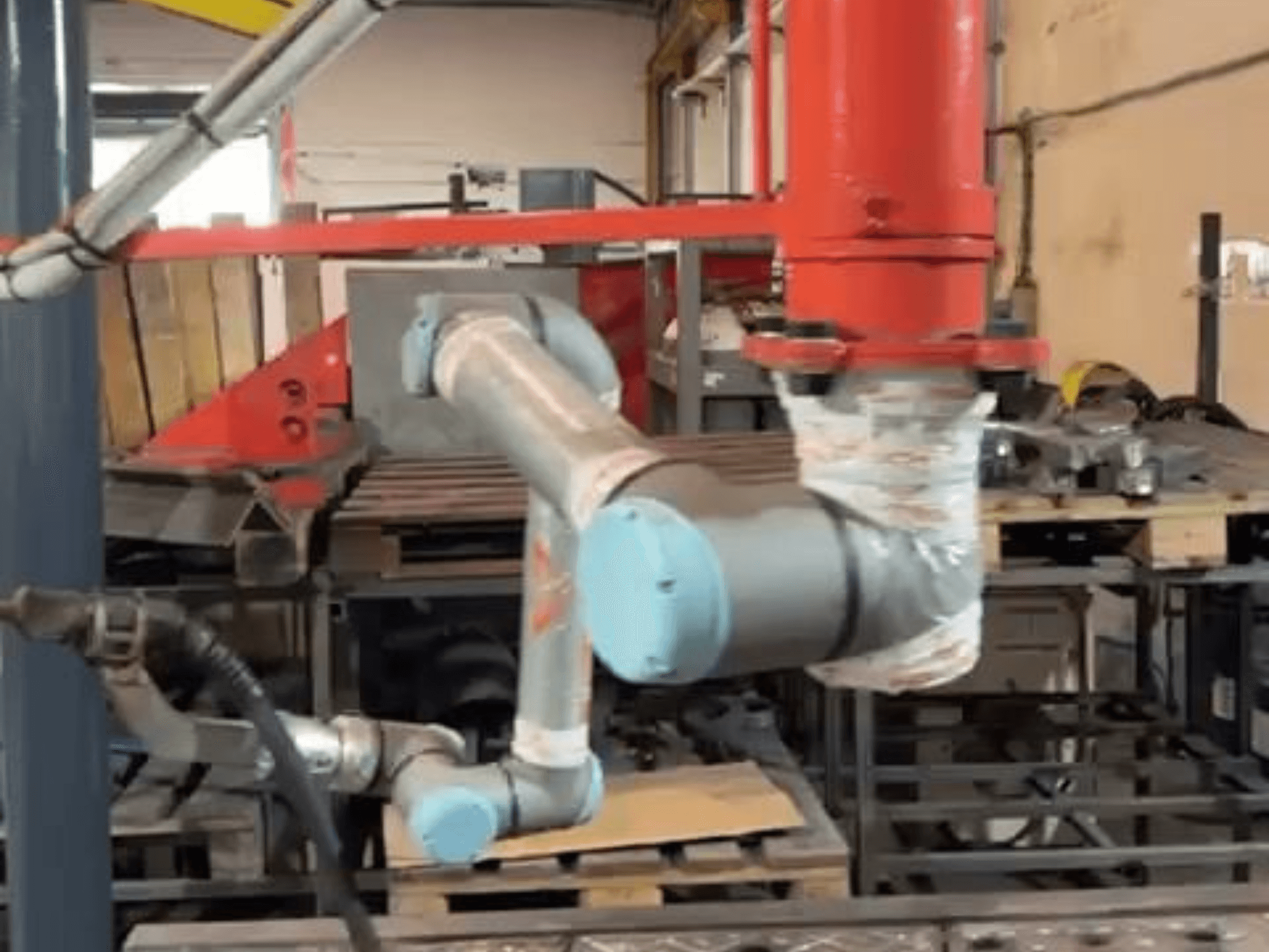 De collaboratieve robot UR10e van Universal Robots in een werkplaats; zijaanzicht waarin de bewegingen van de arm en de gewrichten in de buurt van machines te zien zijn.