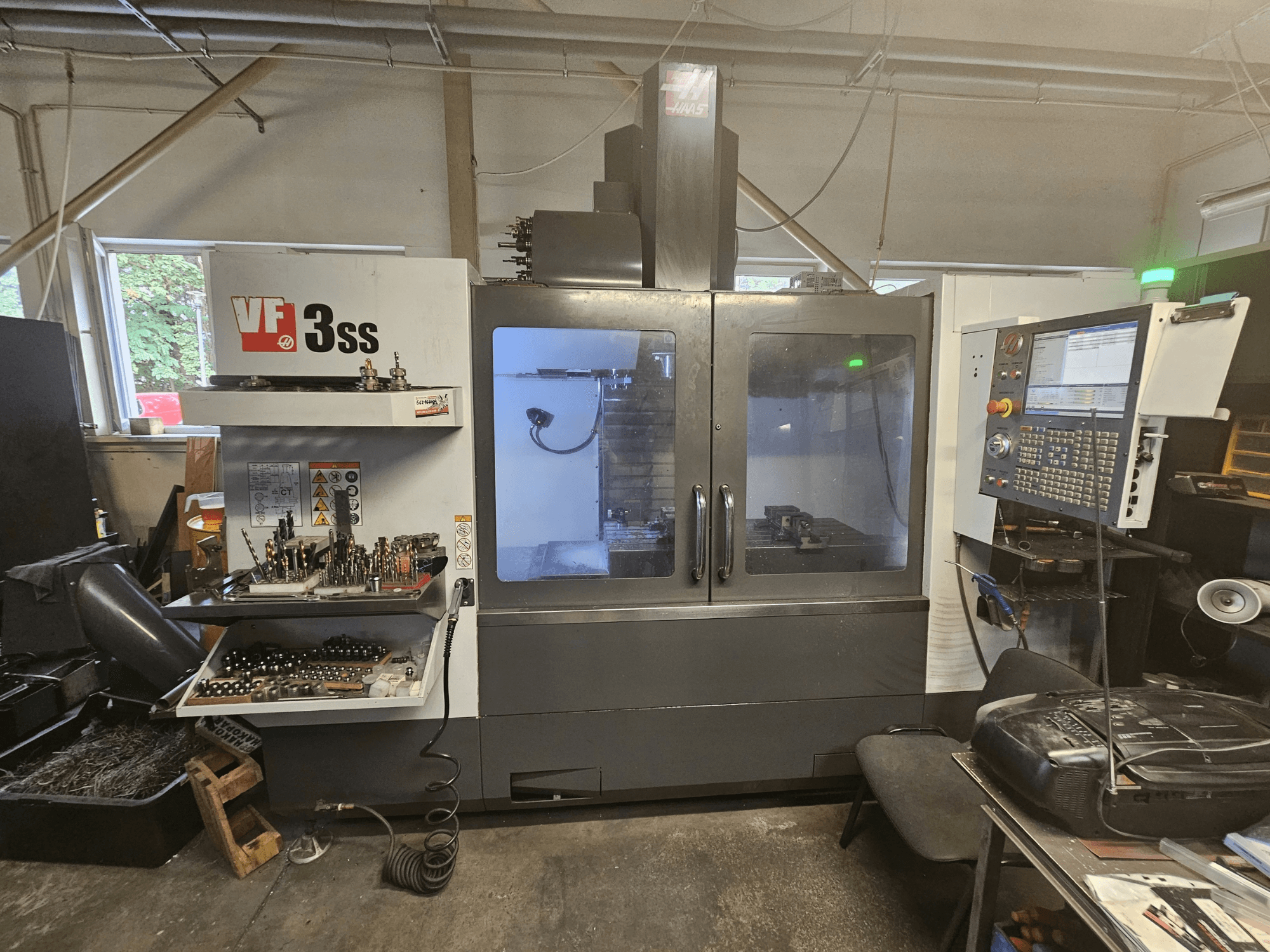 Haas VF-3SS verticaal bewerkingscentrum in een werkplaats, vooraanzicht met bedieningspaneel en gereedschapskast.