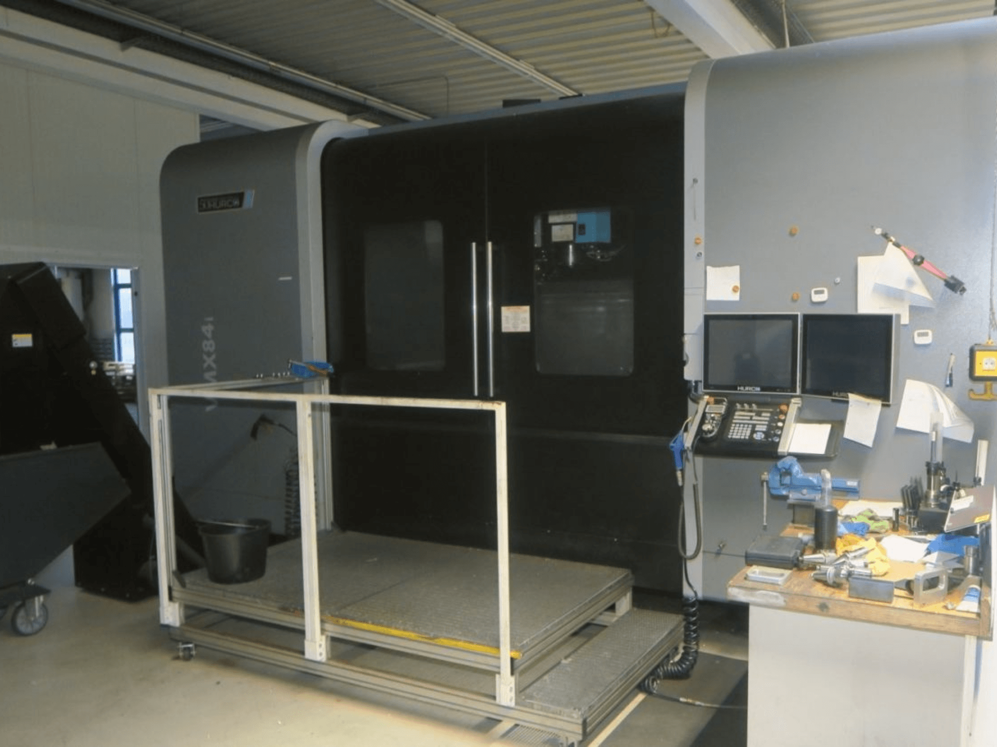 Hurco MX84 CNC machine in vooraanzicht, met dubbele monitoren, bedieningspaneel en werkruimte met diverse gereedschappen.