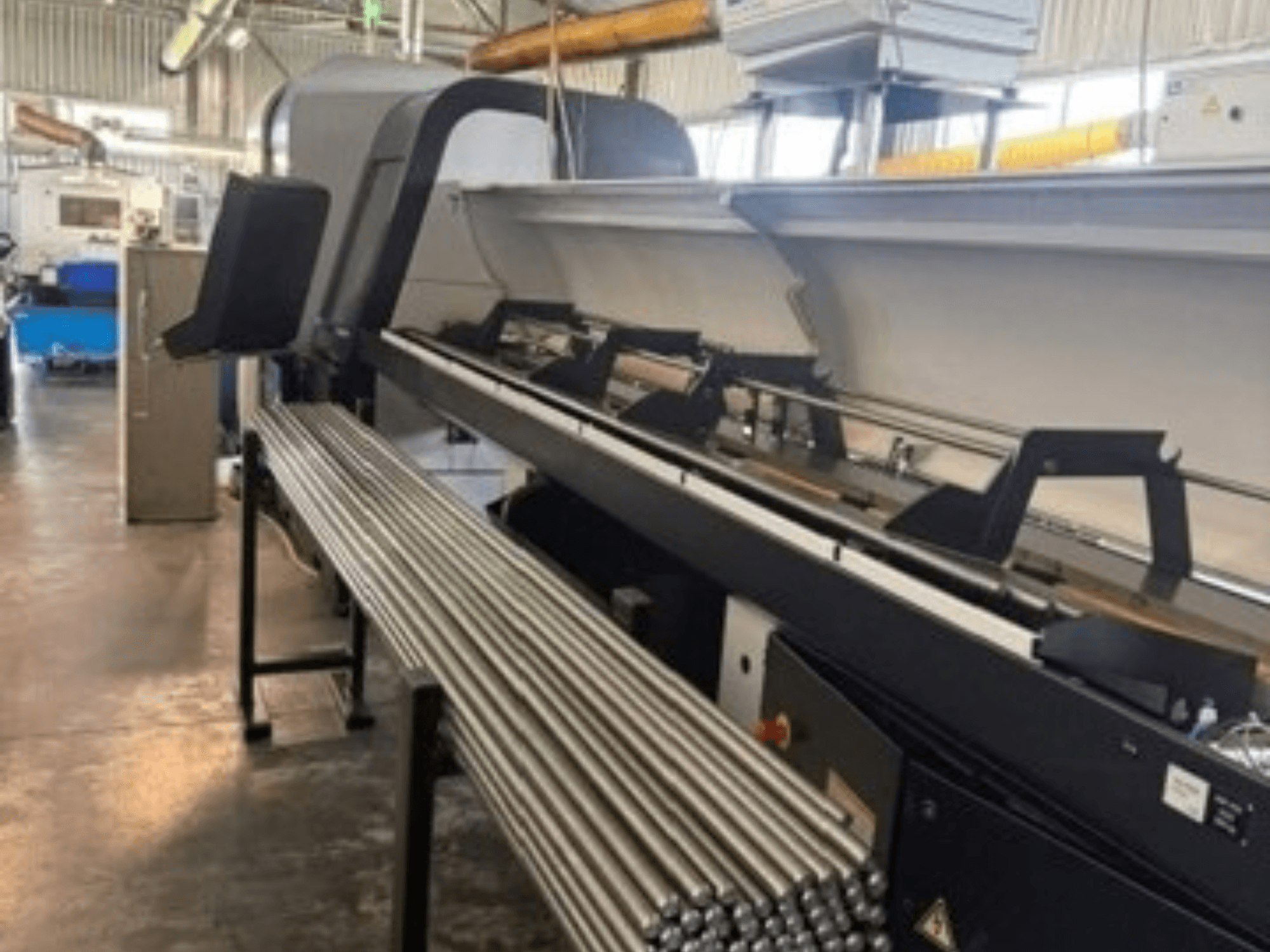 Vooraanzicht van de TORNOS EvoDECO 32, een Zwitserse draaimachine, met daarnaast opgestelde metalen staven, waarmee de industriële werkruimte wordt getoond.