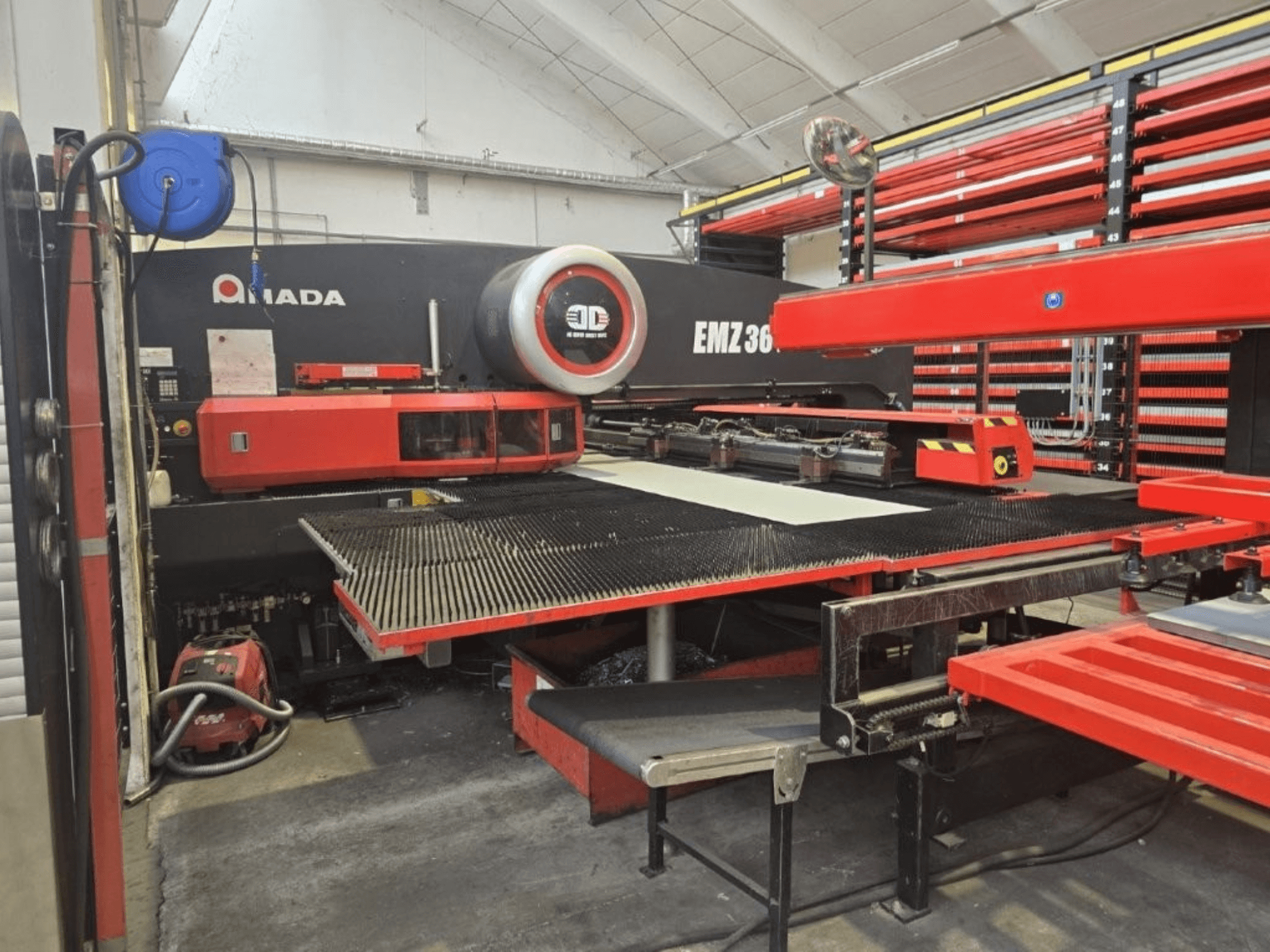 Amada EMZ 36 lasersnijmachine in een werkplaats, vooraanzicht, met rode accenten en een grote snijtafel.