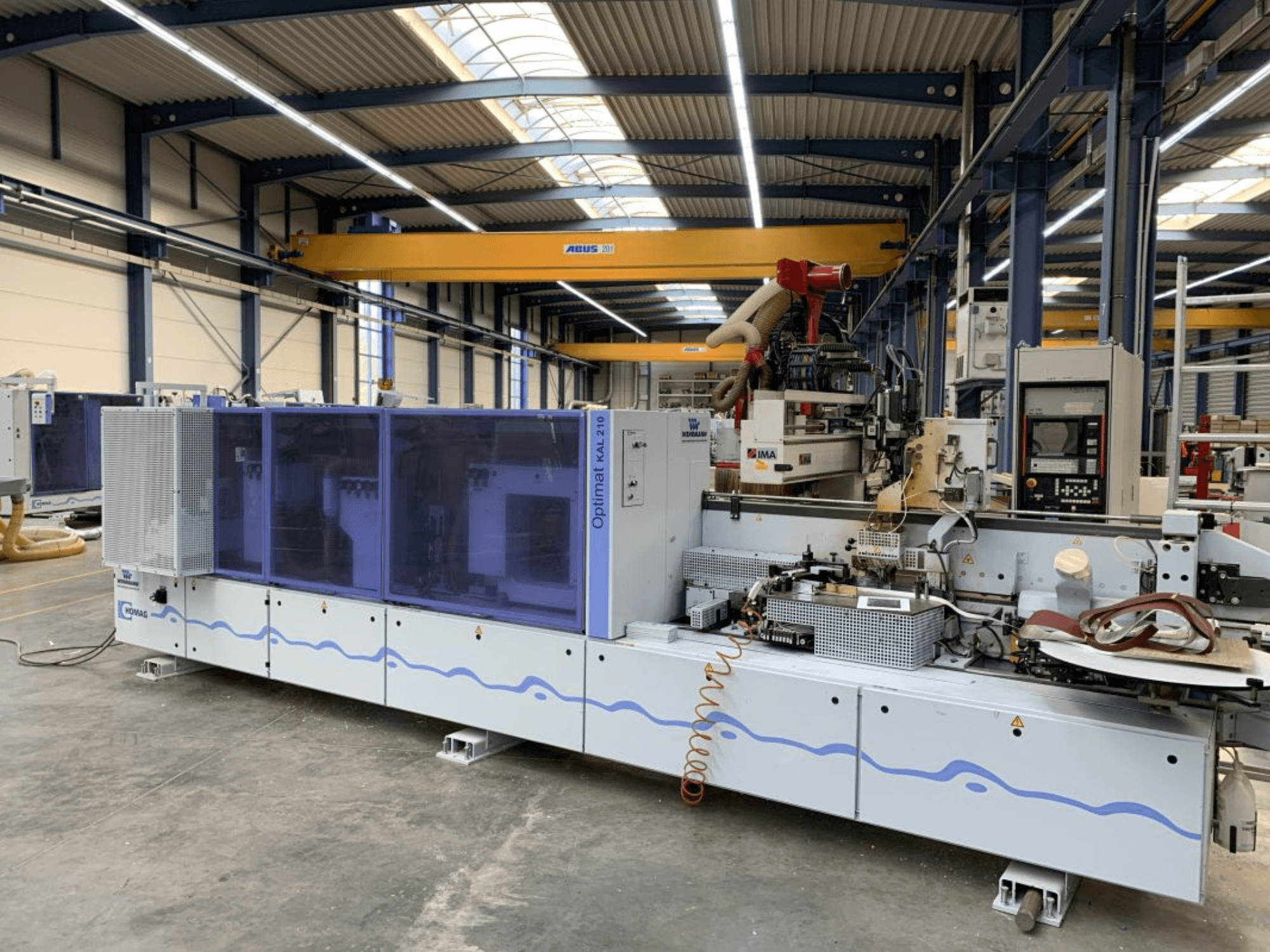De HOMAG Optimat KAL210-kantenlijmmachine in vooraanzicht, waarbij het bedieningspaneel en het bewerkingsgebied in een fabrieksomgeving te zien zijn.