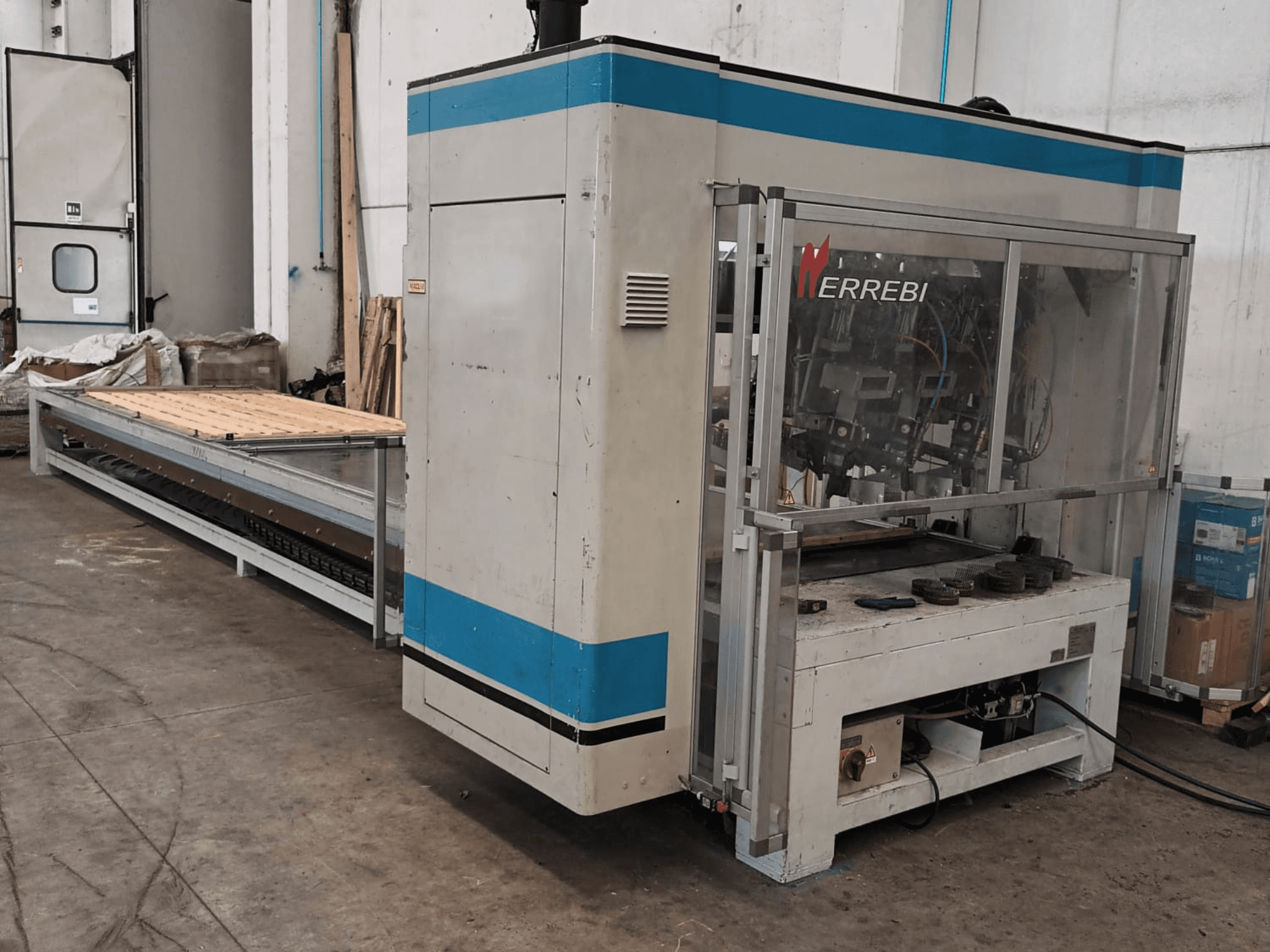ERREBI machine, zijaanzicht, heeft een grote verwerkingstafel met mechanische onderdelen en transparante beschermkap.