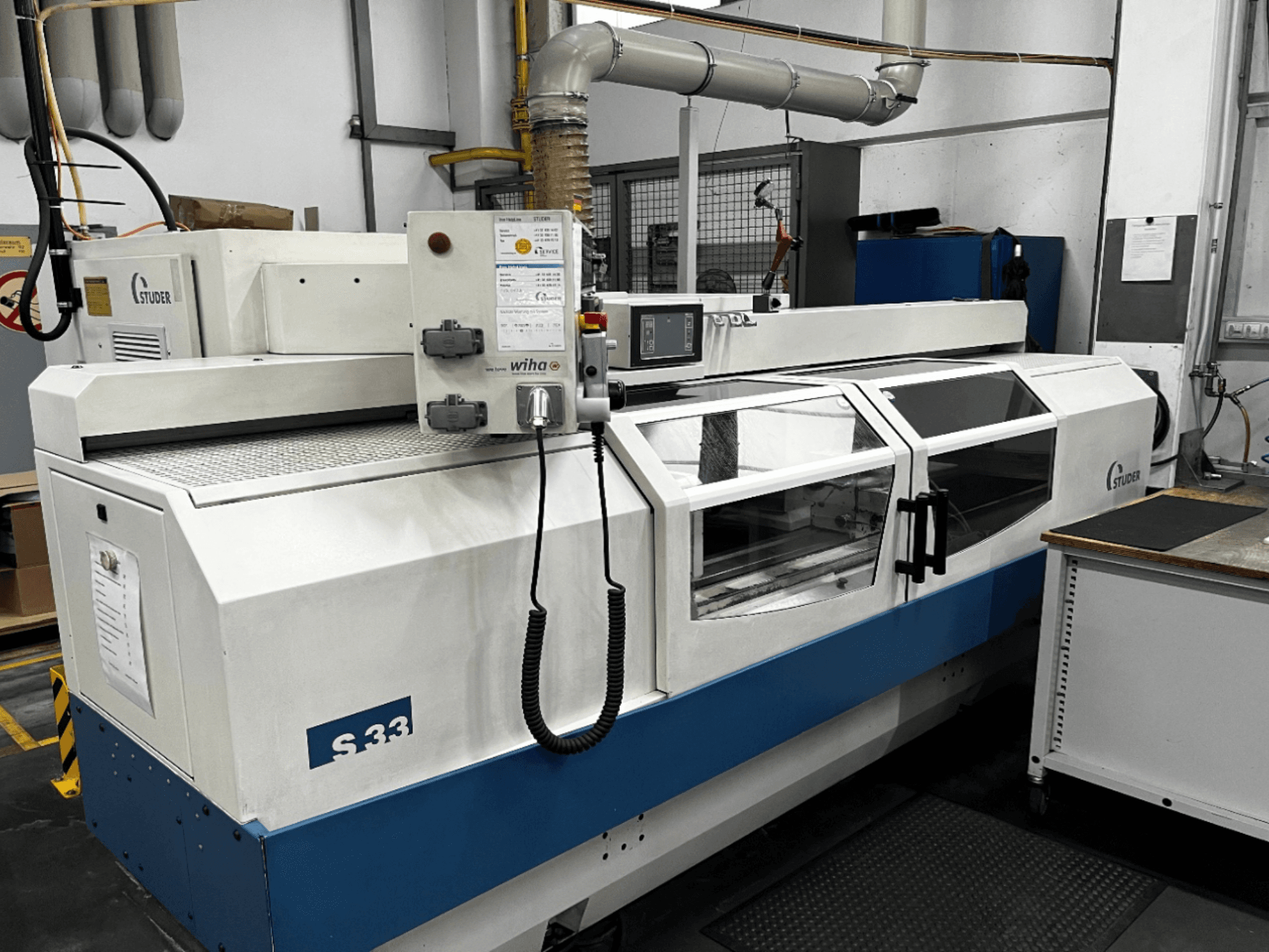 STUDER S33 CNC rondslijpmachine, vooraanzicht; voorzien van bedieningspaneel en glazen veiligheidsdeuren. Industriële omgeving.