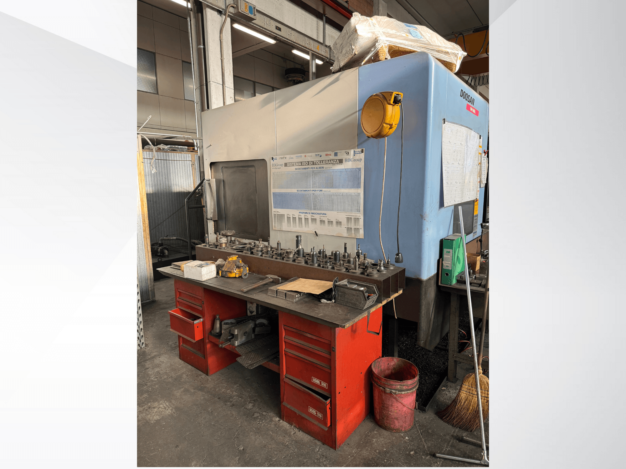 Doosan bewerkingscentrum met een rode werkbank en opslag, waar gereedschap en apparatuur worden getoond, gezien vanaf de voorkant.