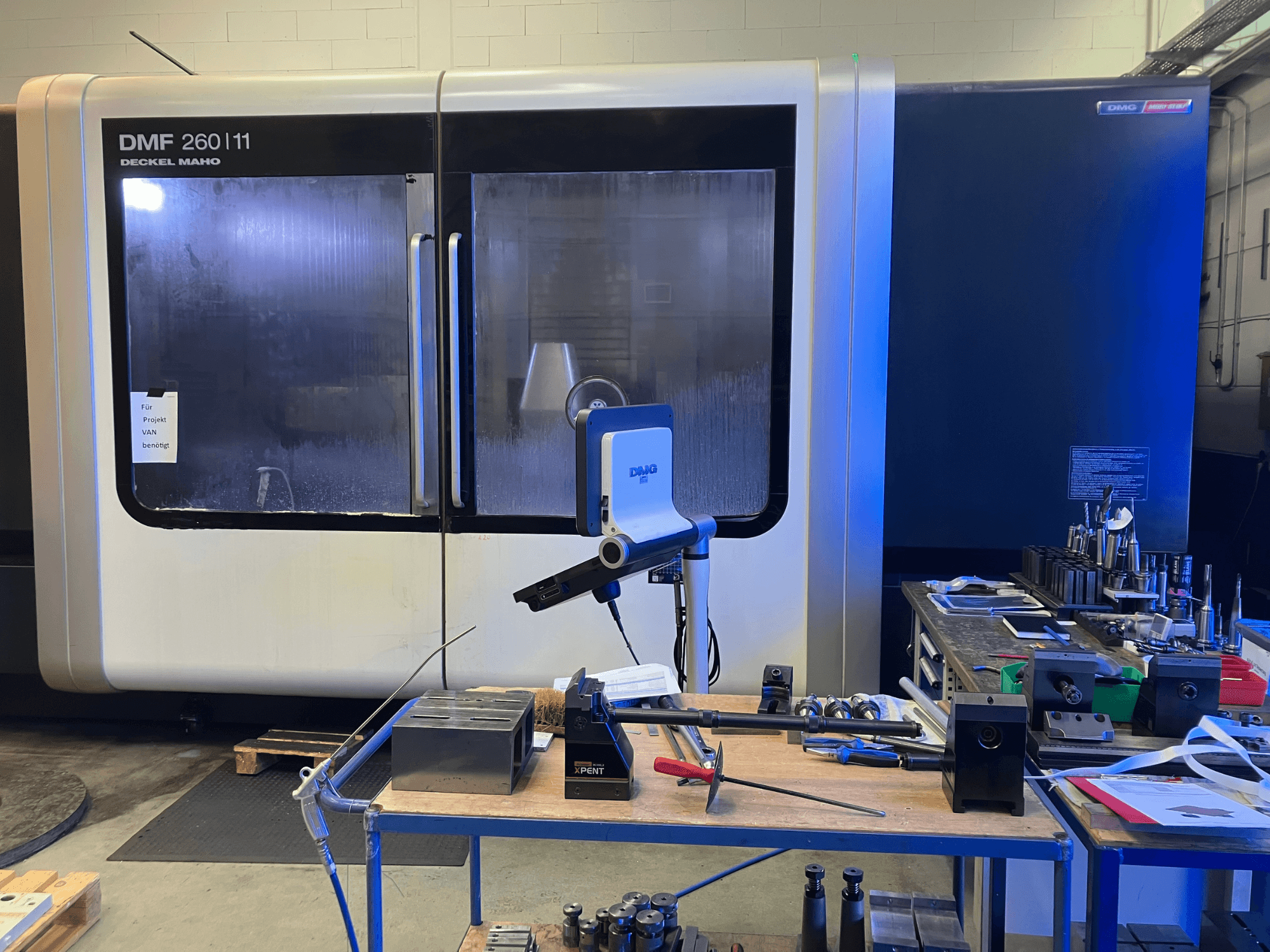 Vooraanzicht van DMG DECKEL MAHO DMF 260|11 verticaal bewerkingscentrum met gereedschappen en materialen op een werkstation.