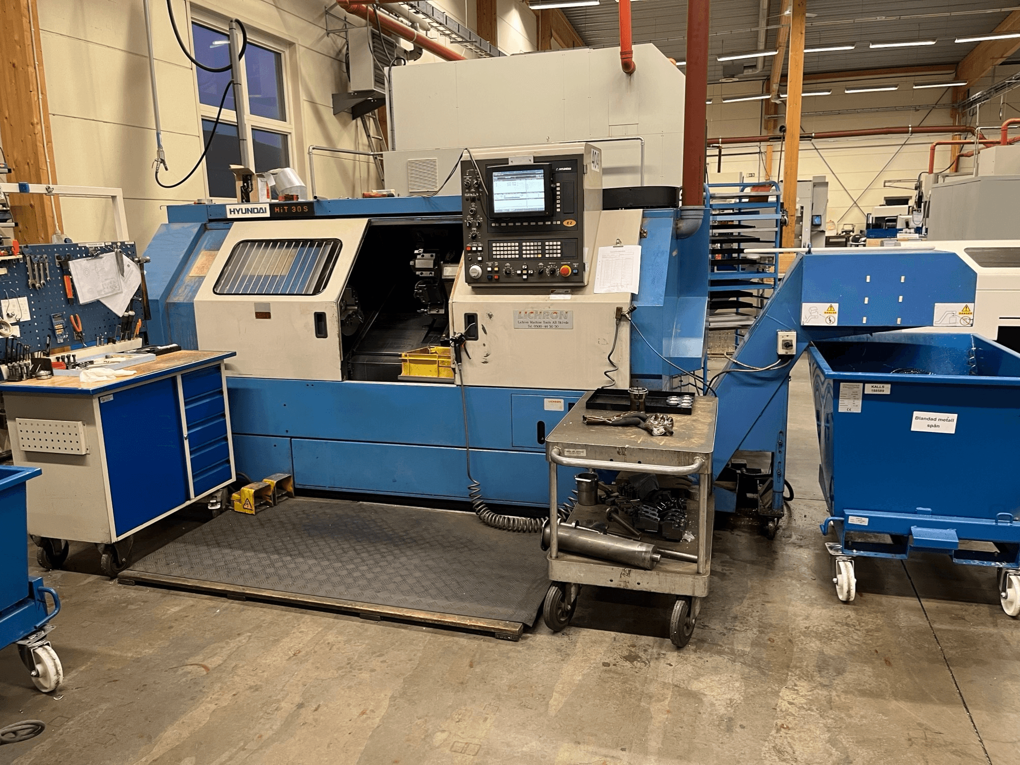 Hyundai HIT 30S horizontale draaimachine, vooraanzicht, met bedieningspaneel en gereedschap op een nabijgelegen kar in een werkplaats.