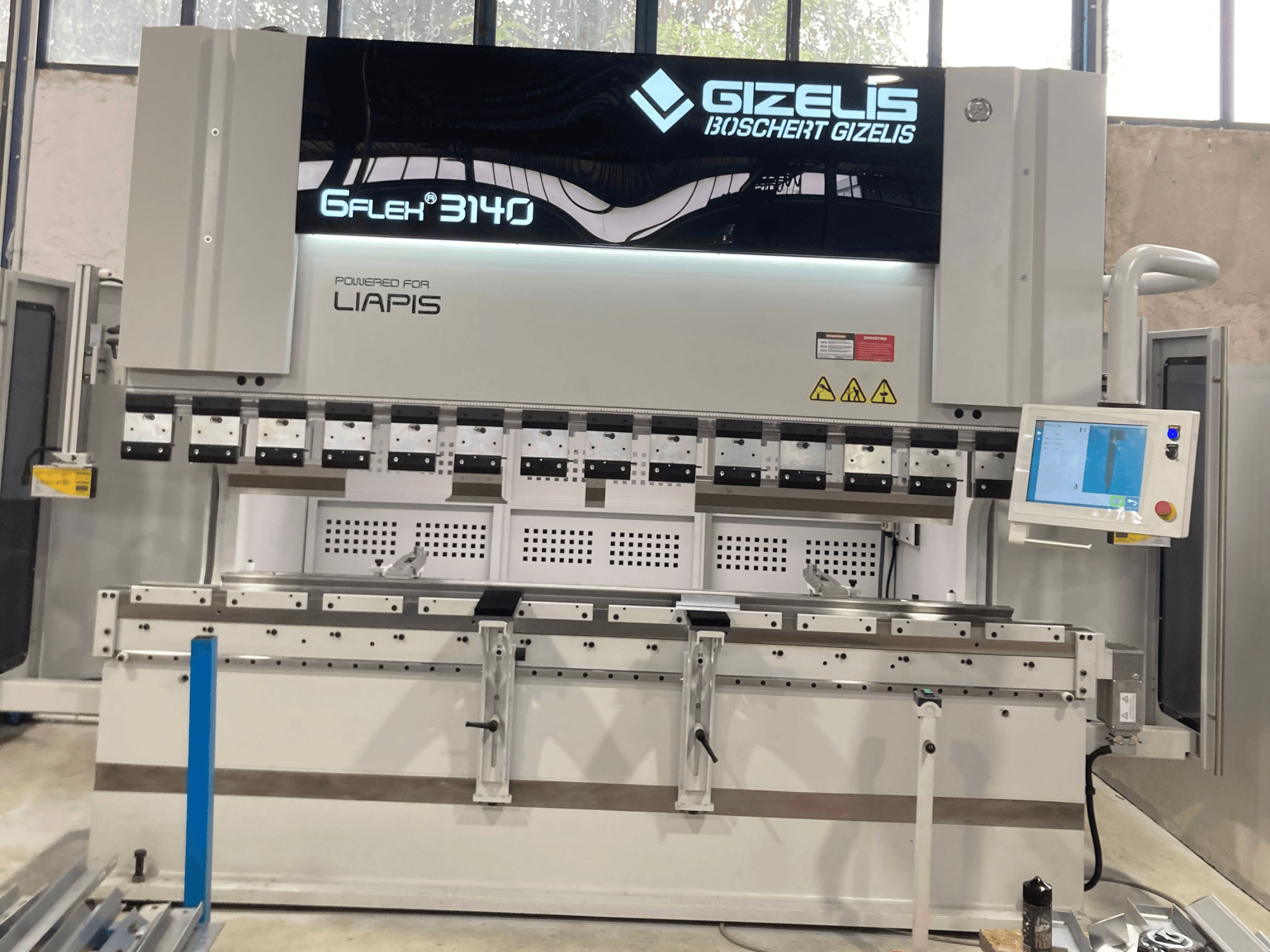 Hydraulische pers GIZELIS G-FLEX 3140 in vooraanzicht met bedieningsscherm, voorzien van meerdere buiggereedschappen en veiligheidslabels.