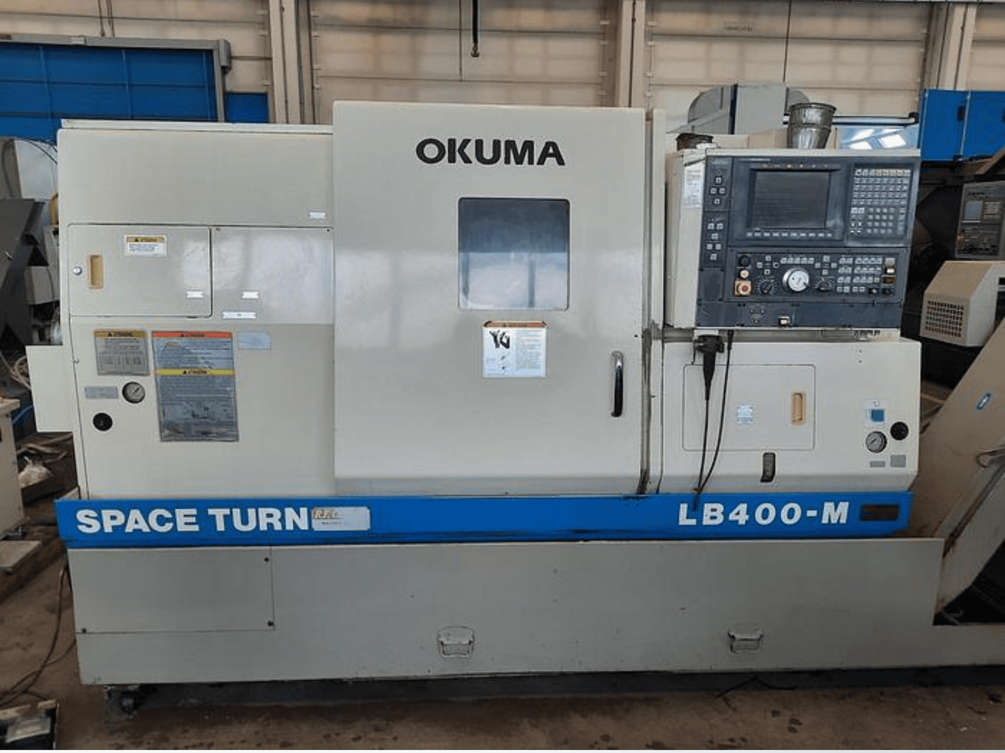 Okuma LB400-M CNC draaibank, vooraanzicht met bedieningspaneel, waarschuwingslabels en blauw "SPACE TURN" opschrift zichtbaar.