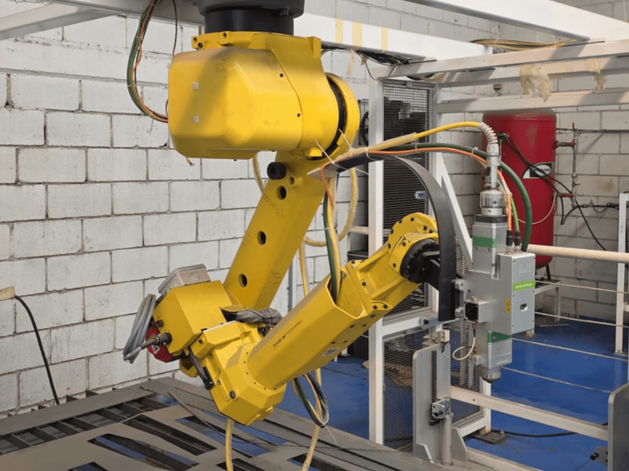 Gele robotarm met een precisiegereedschap, met meerdere gewrichten en kabels, gezien vanaf de voorkant in een industriële omgeving.