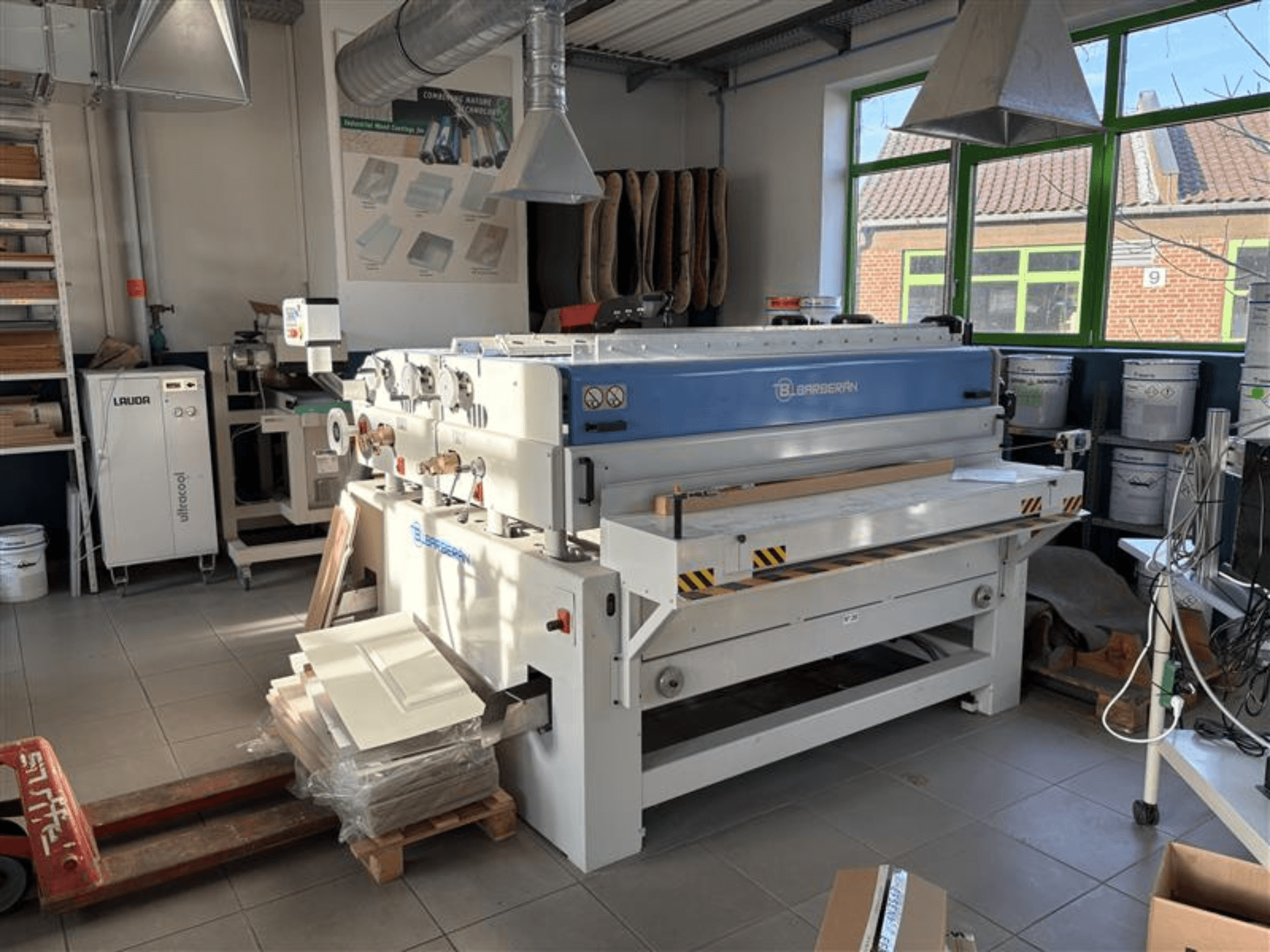 Blaserbn houtbewerkingsmachine in een werkplaats, vooraanzicht; met houten panelen op een pallet en moderne apparatuur op de achtergrond.