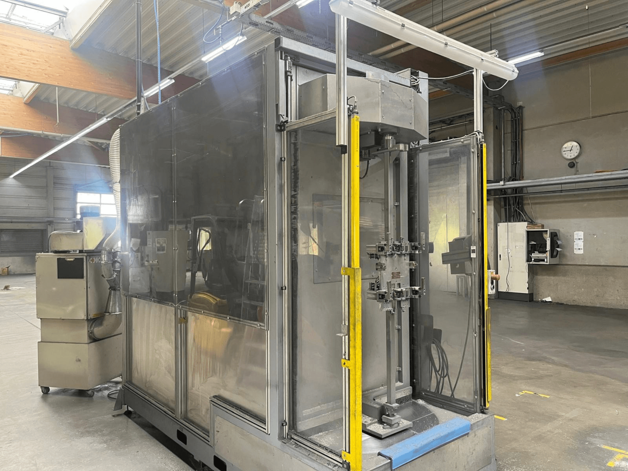 Een M.A.I. ASD 1-bewerkingsmachine, gezien vanuit de zijkant, met een doorzichtige behuizing en bedieningselementen aan de voorzijde in een werkplaats.