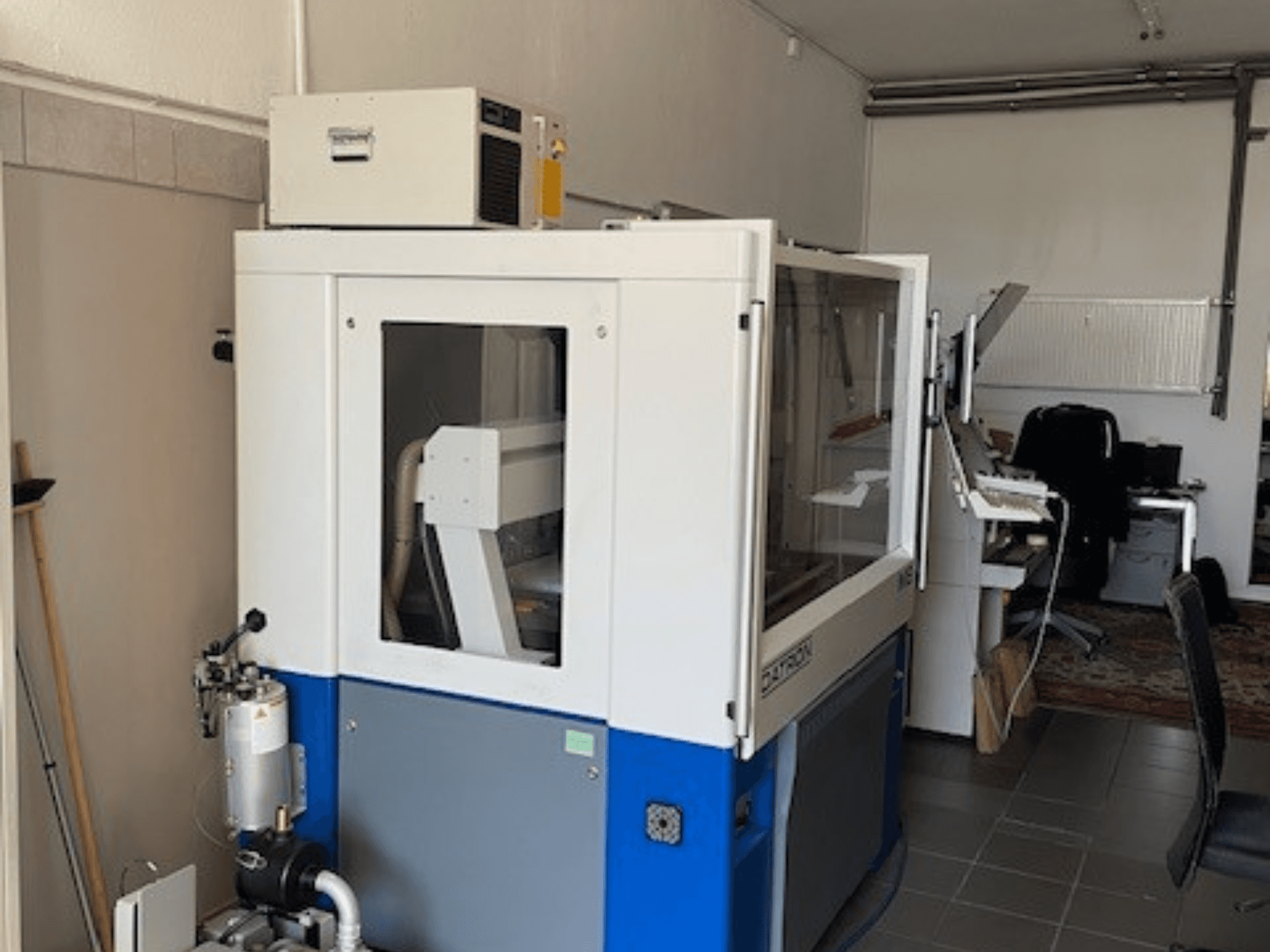 Blauw-witte industriële machine met transparante panelen, vooraanzicht, inclusief toegang voor bediening en zichtbare ventilatie-eenheid.