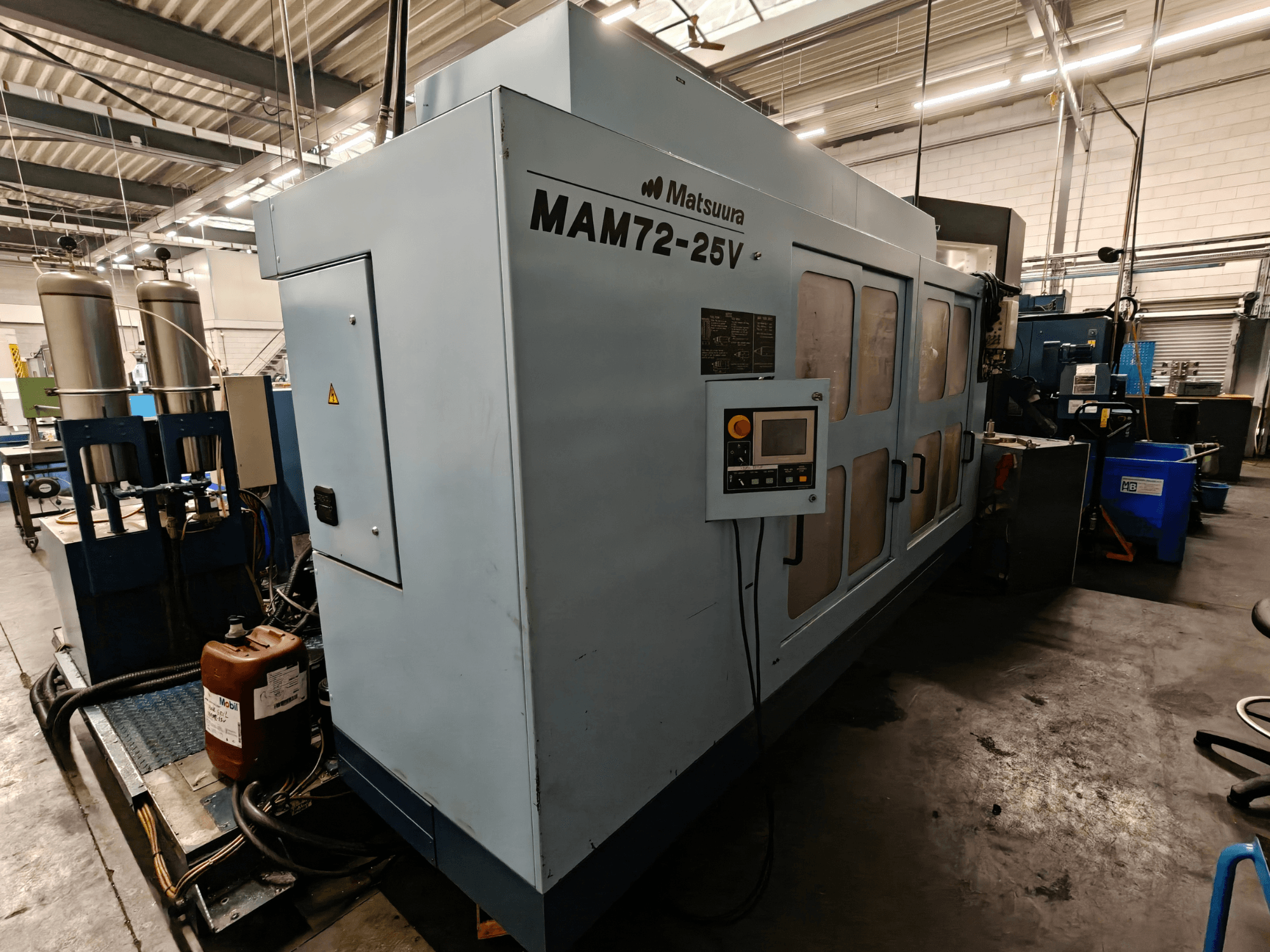 Matsuura MAM72-25V CNC machine, zijaanzicht, met bedieningspaneel, dubbele koelvloeistoftanks en werkruimte in een industriële omgeving.