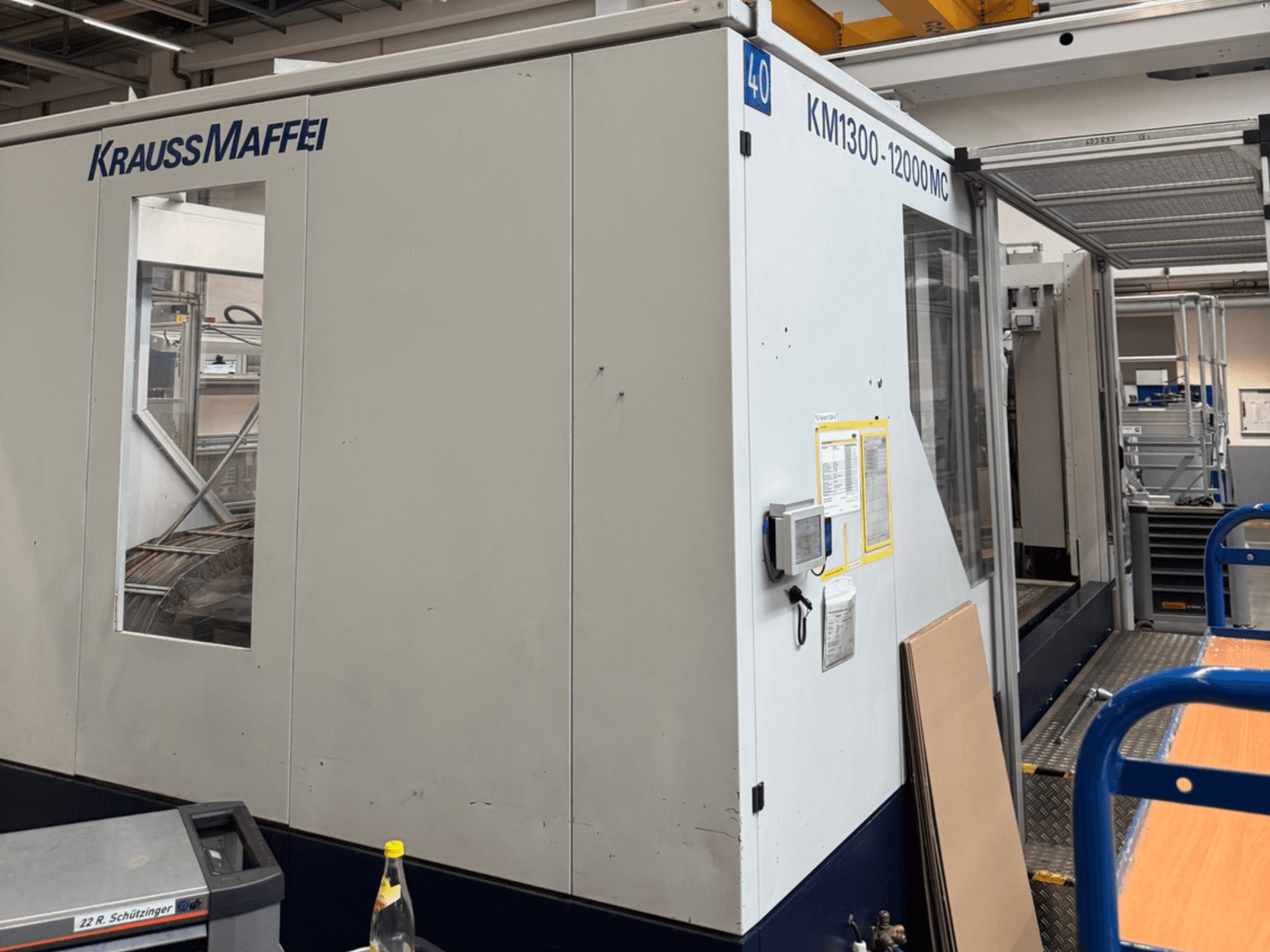 Krauss Maffei hydraulische spuitgietmachine KM1300-12000 MC, zijaanzicht, met het bedieningspaneel en de werkruimte.