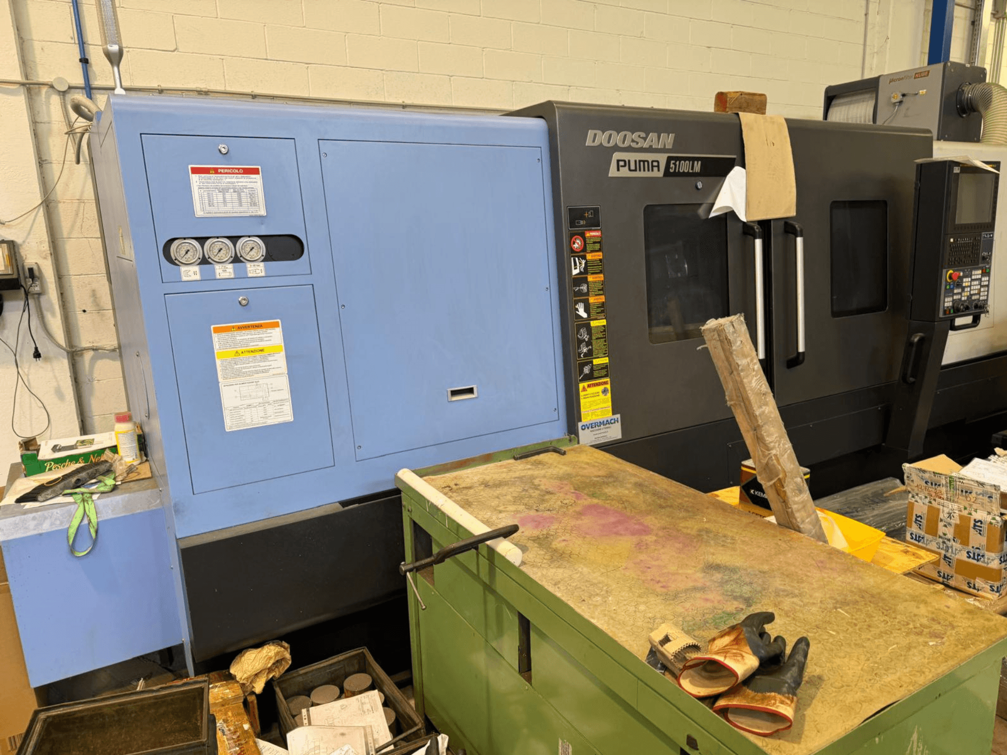 Doosan Puma 5100LM CNC machine en bedieningspaneel, zijaanzicht. Meters en waarschuwingslabels zichtbaar op de blauwe besturingseenheid.