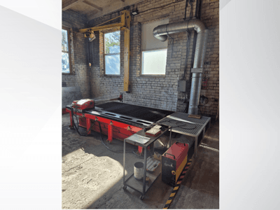 Rode CNC-plasmasnijtafel met bedieningspaneel en metalen afzuigkanaal, gezien vanaf de zijkant in een goed verlichte werkplaats.