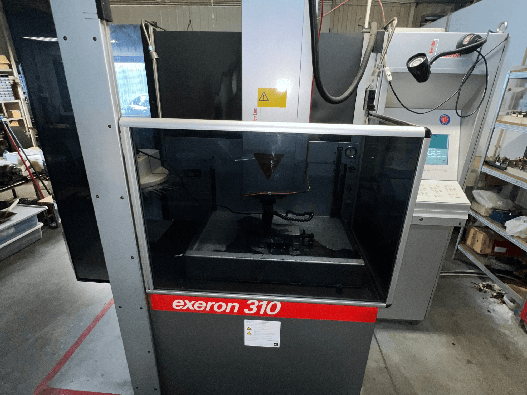 Vooraanzicht van een Exeron 310 machine, met een glazen kamer en bedieningspaneel naast werkstationrekken.